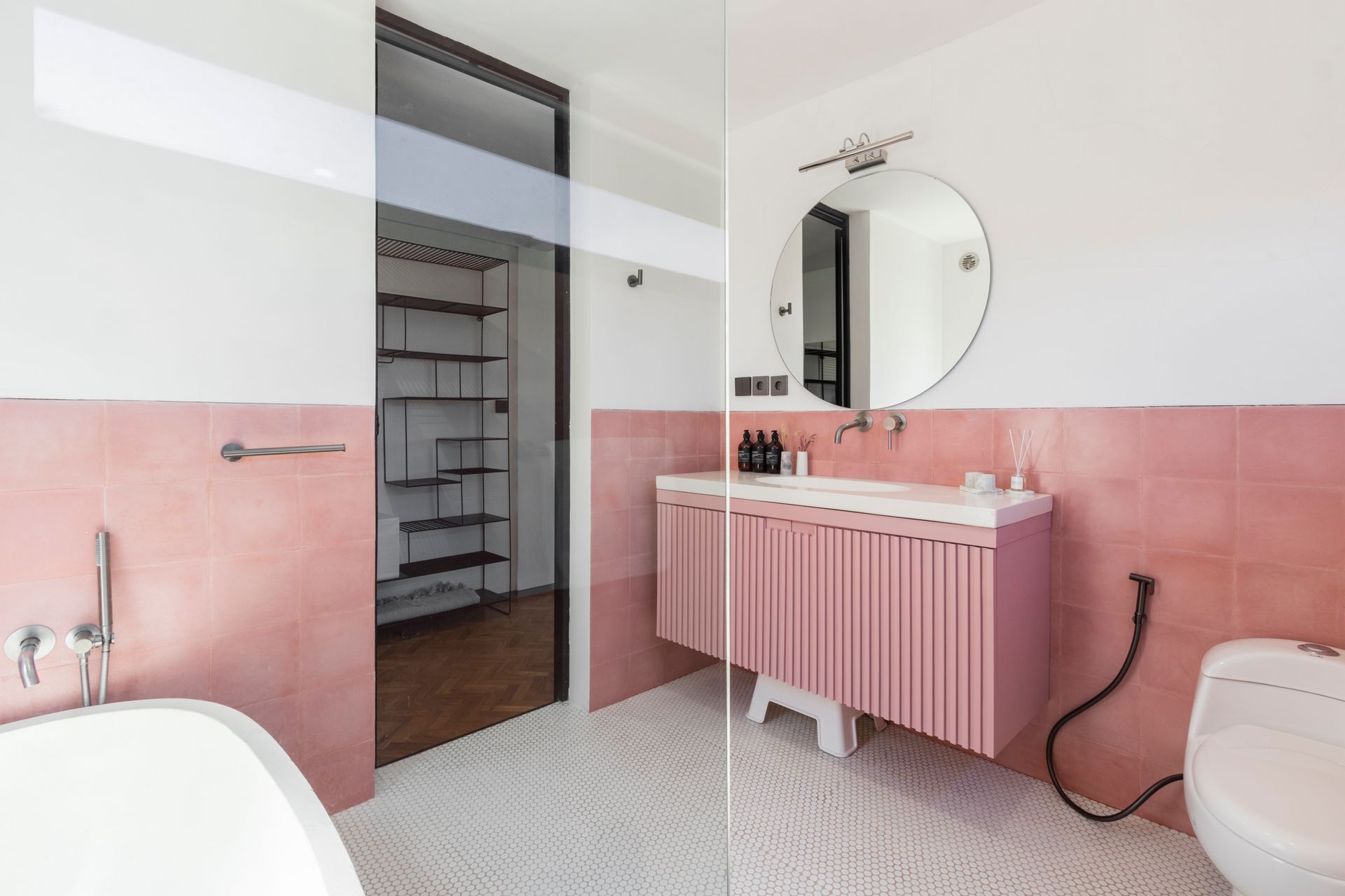 Pink and white bathroom with a floating vanity, round mirror, and a black-framed doorway to shelving.