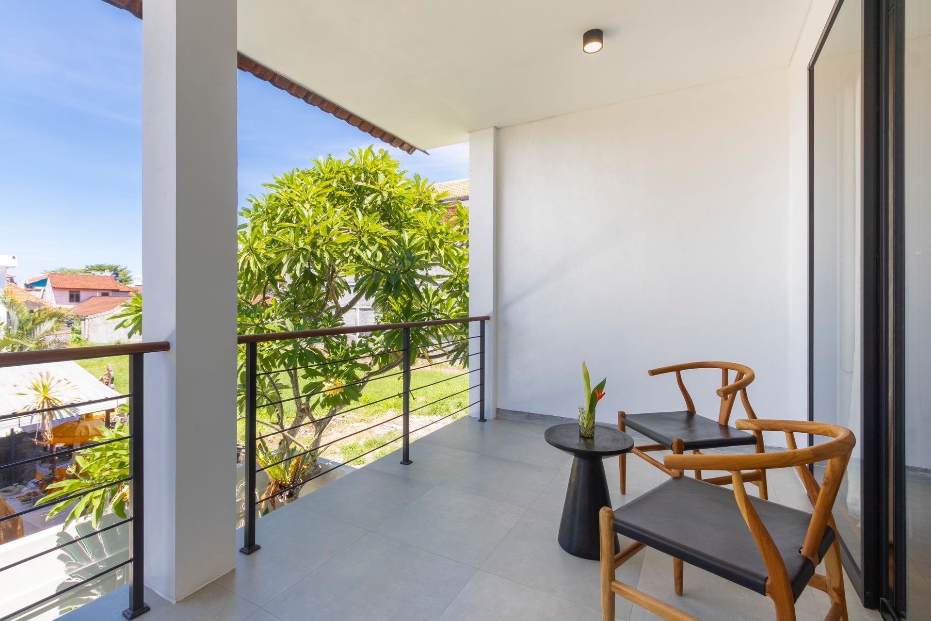 Balcony with two chairs, small table, and railing overlooking trees and buildings. Sunny day.