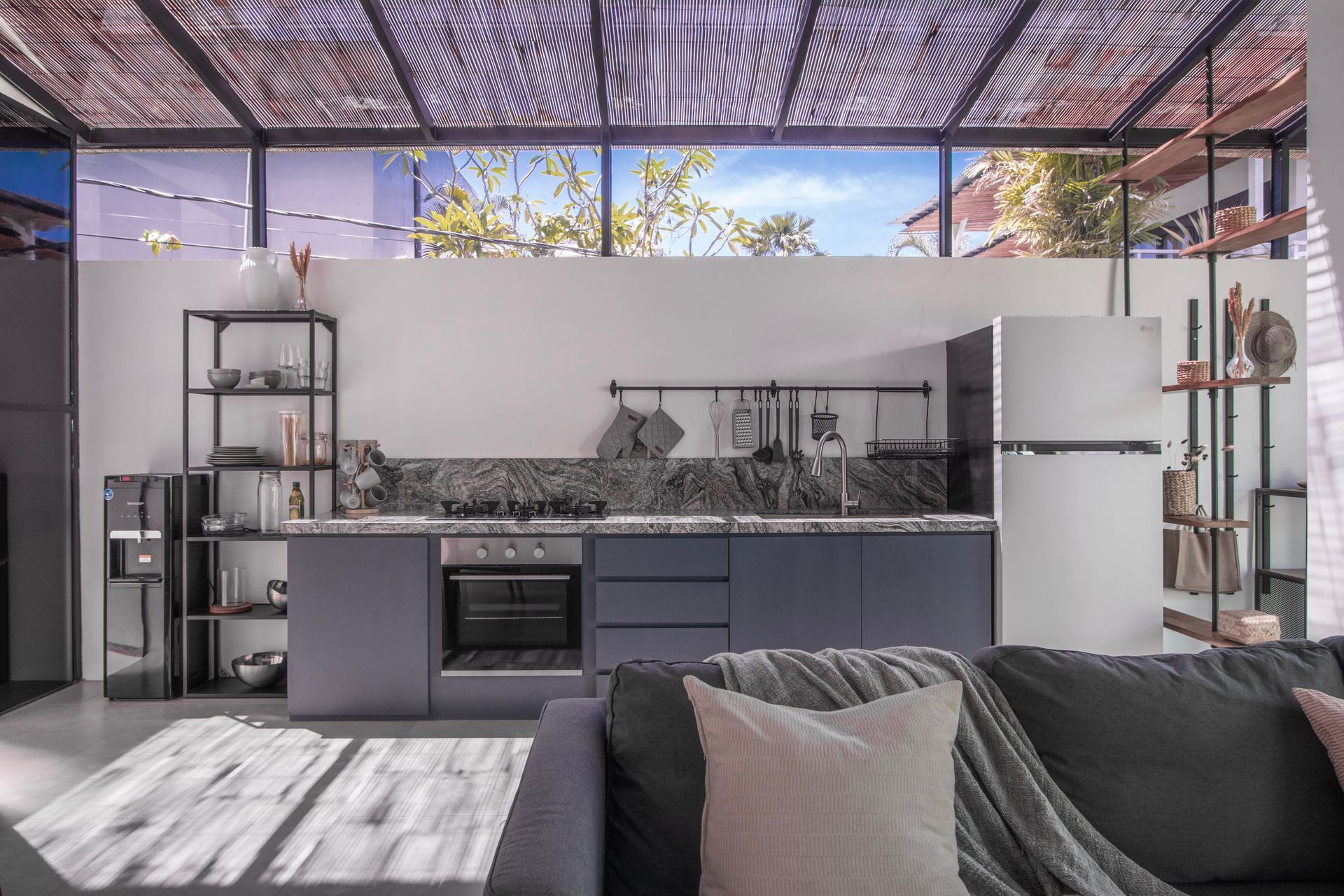 Modern kitchen with grey cabinets, marble backsplash, stainless appliances, and open-air ceiling.
