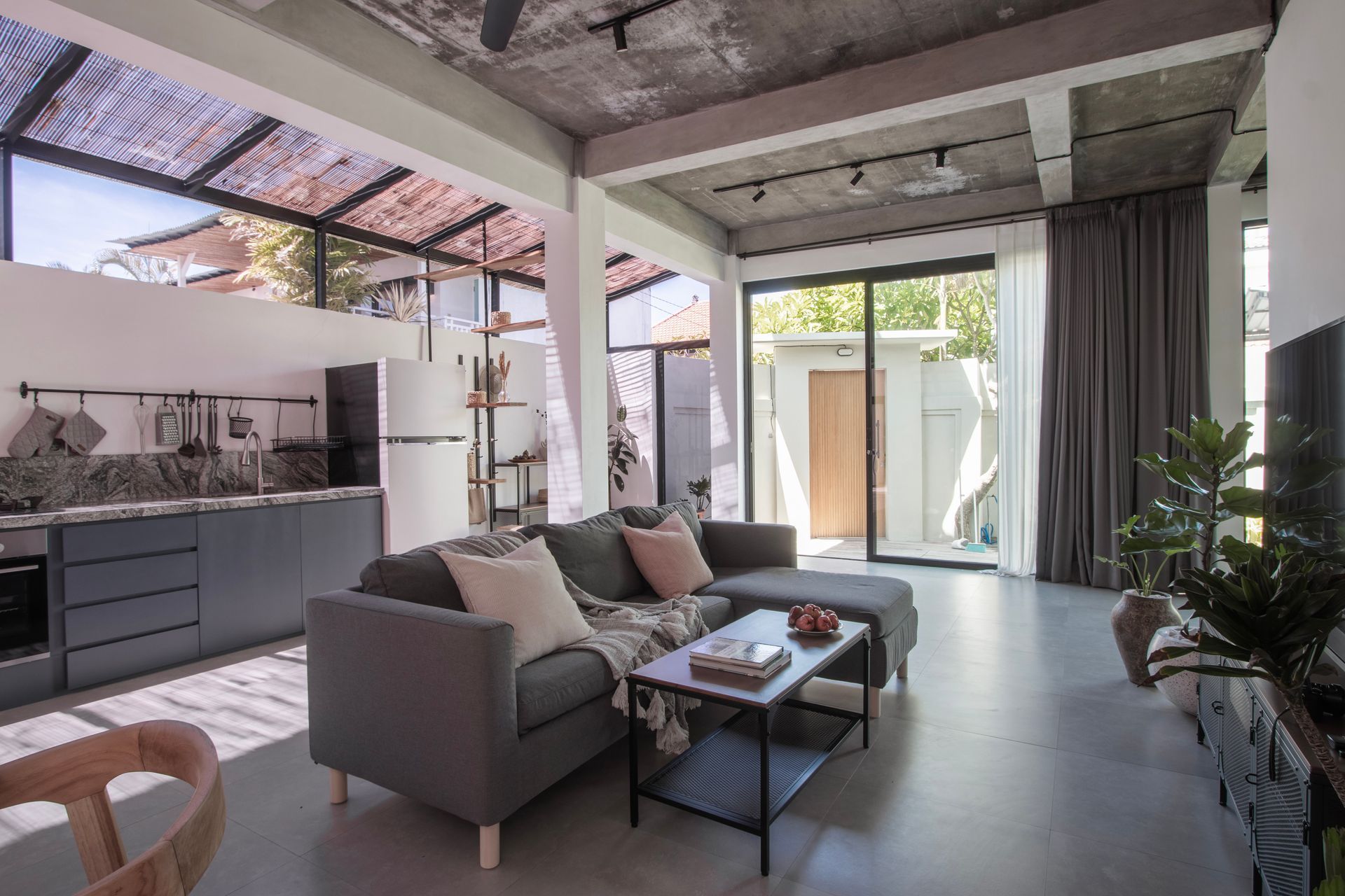 Modern living room with gray sofa, kitchen, and open-air view through a glass door.
