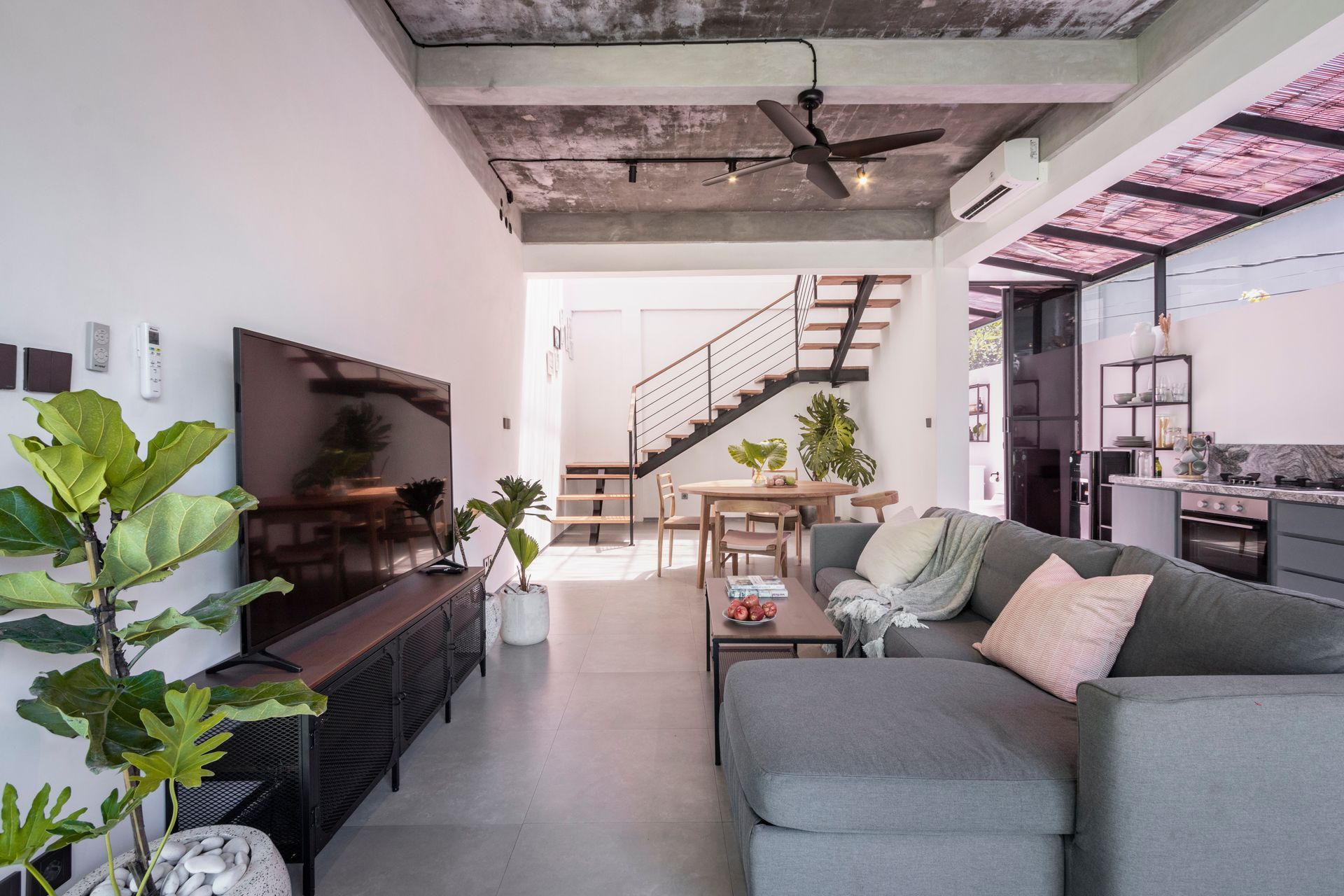 Modern living room with grey sofa, wooden TV stand, and staircase in the background.