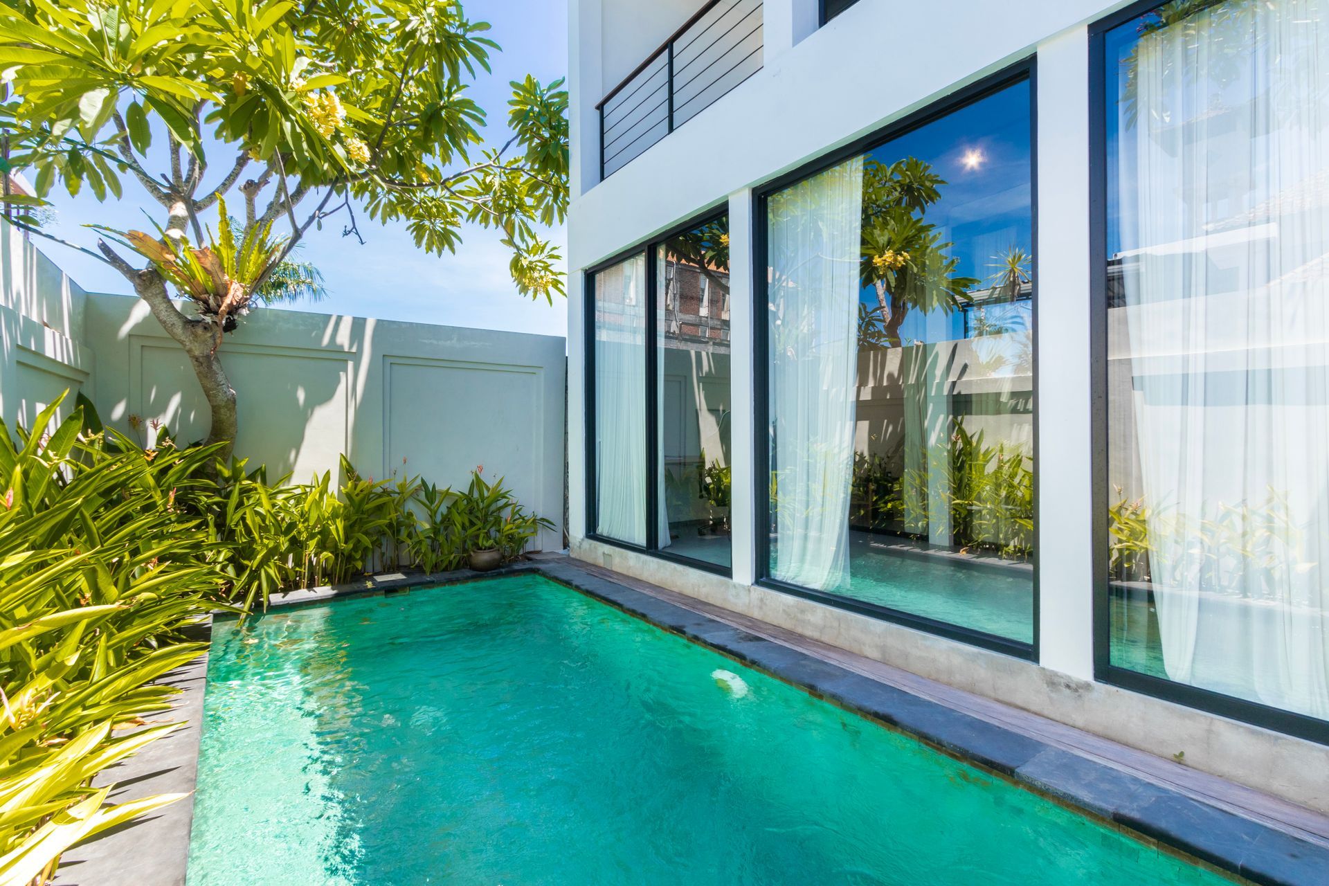 A small pool in front of a modern white building with large windows reflecting greenery.
