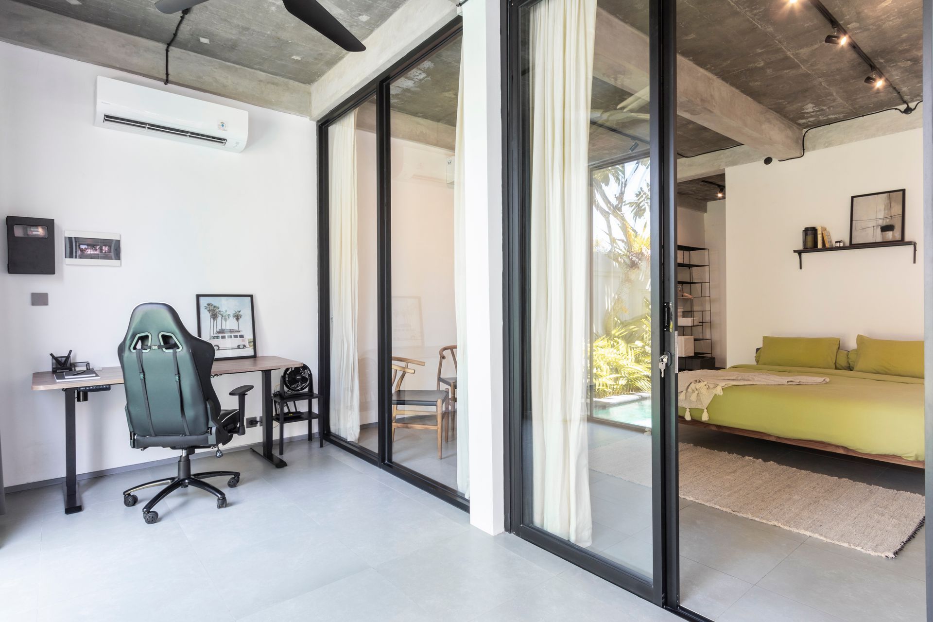 A modern room with glass doors, a desk, a bed, and a view of greenery.