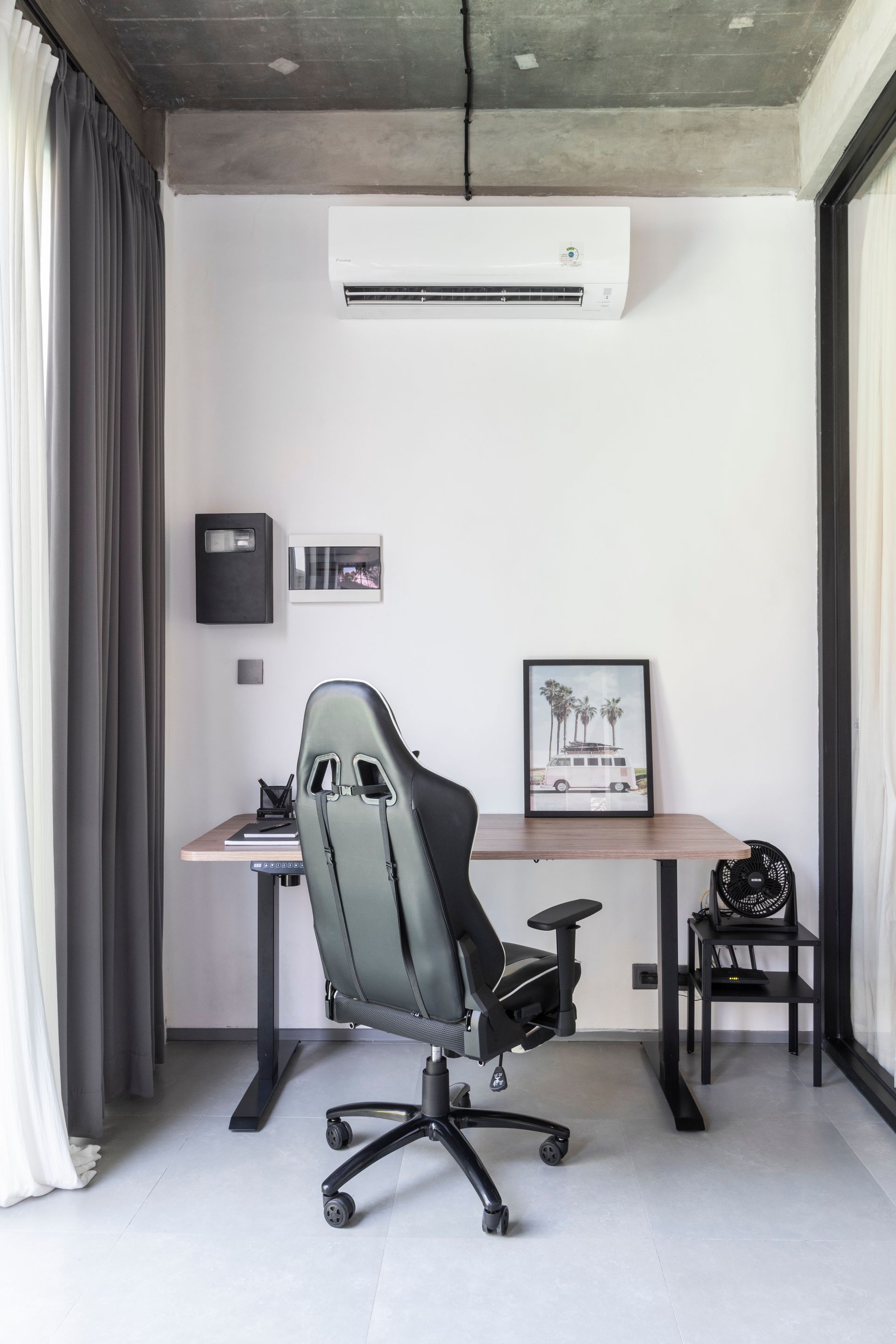 Office space with desk, gaming chair, and small chair against a white wall; air conditioner above.