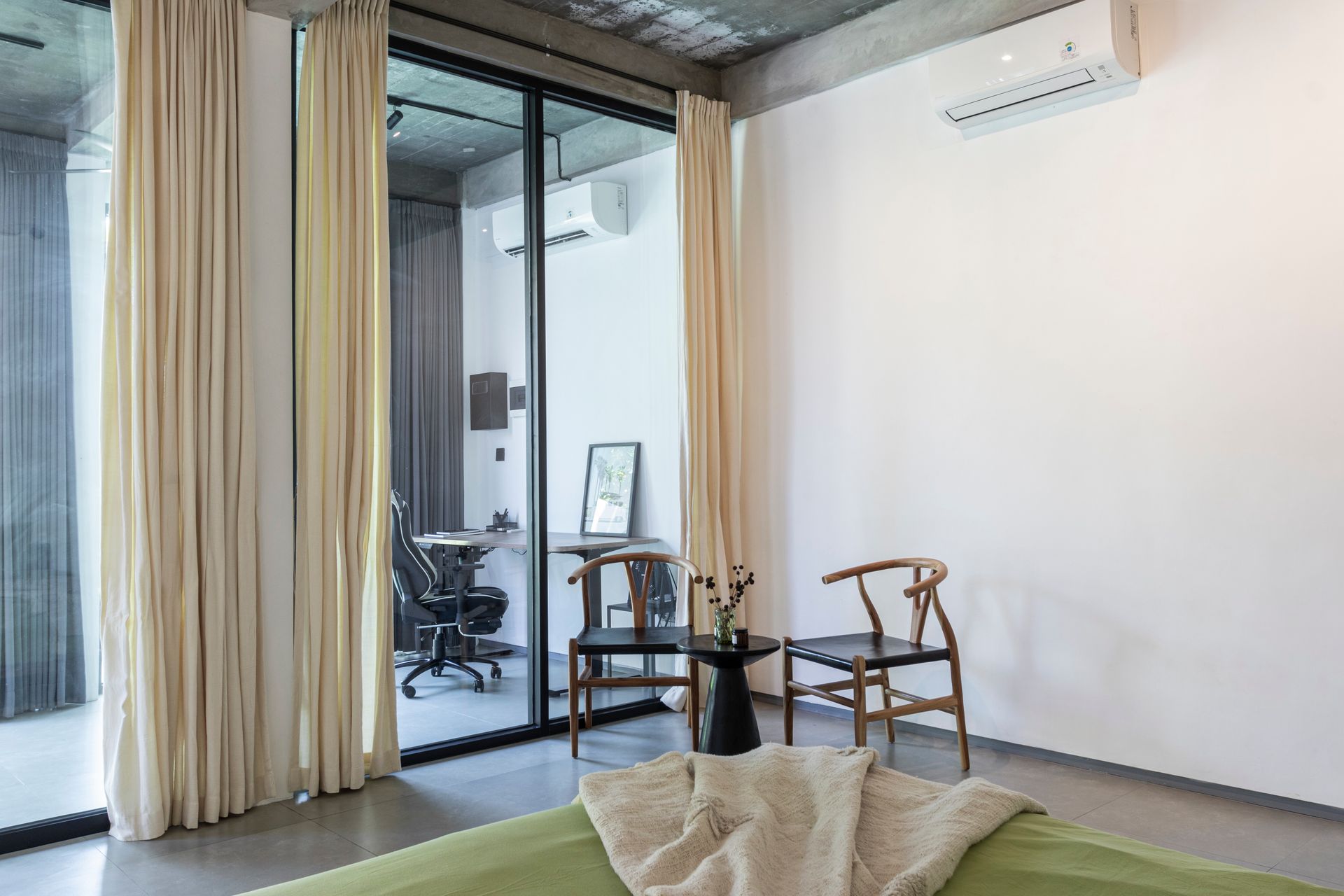 Interior of a modern room with large glass doors and white curtains. Two wooden chairs and a small table sit in front of the window.