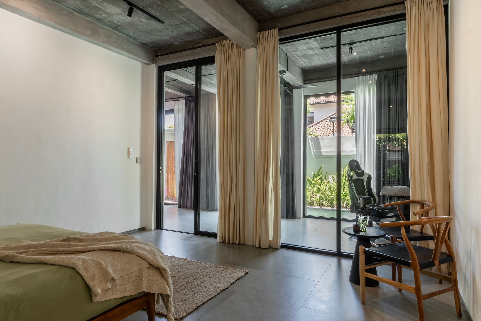 Bedroom with concrete ceiling, large glass doors, sheer curtains, and wooden furniture.