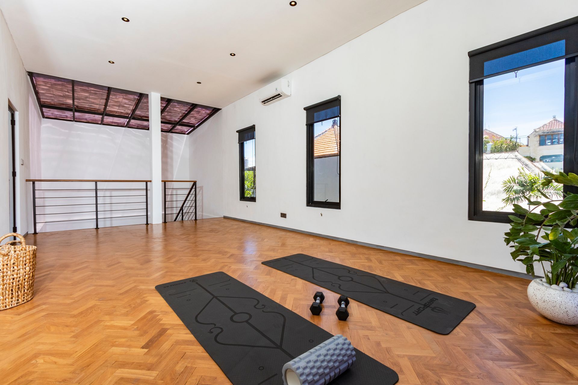 Yoga studio with wooden floor, mats, kettlebells, and large windows.