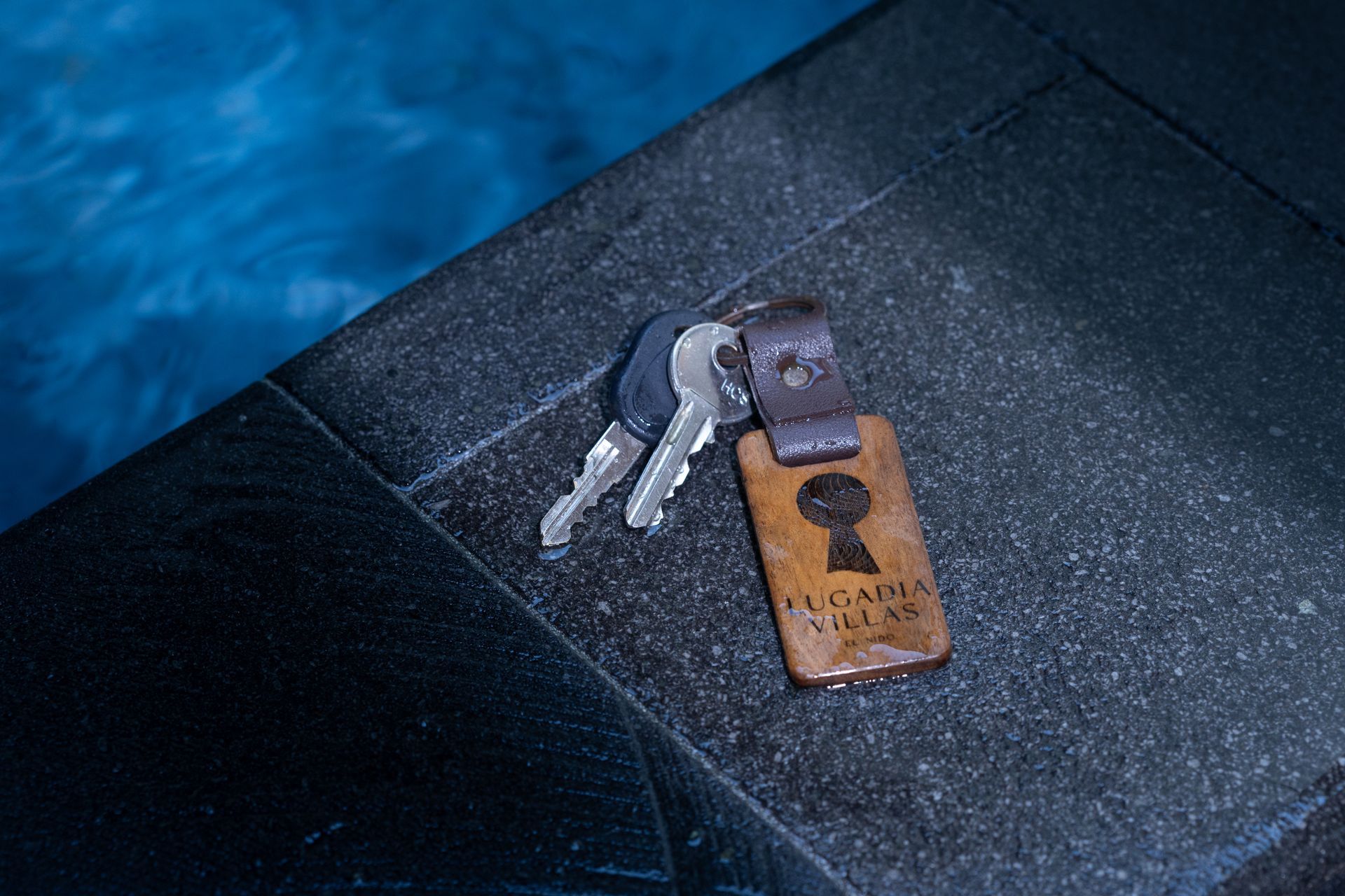 Keys with a wooden key tag next to a pool.