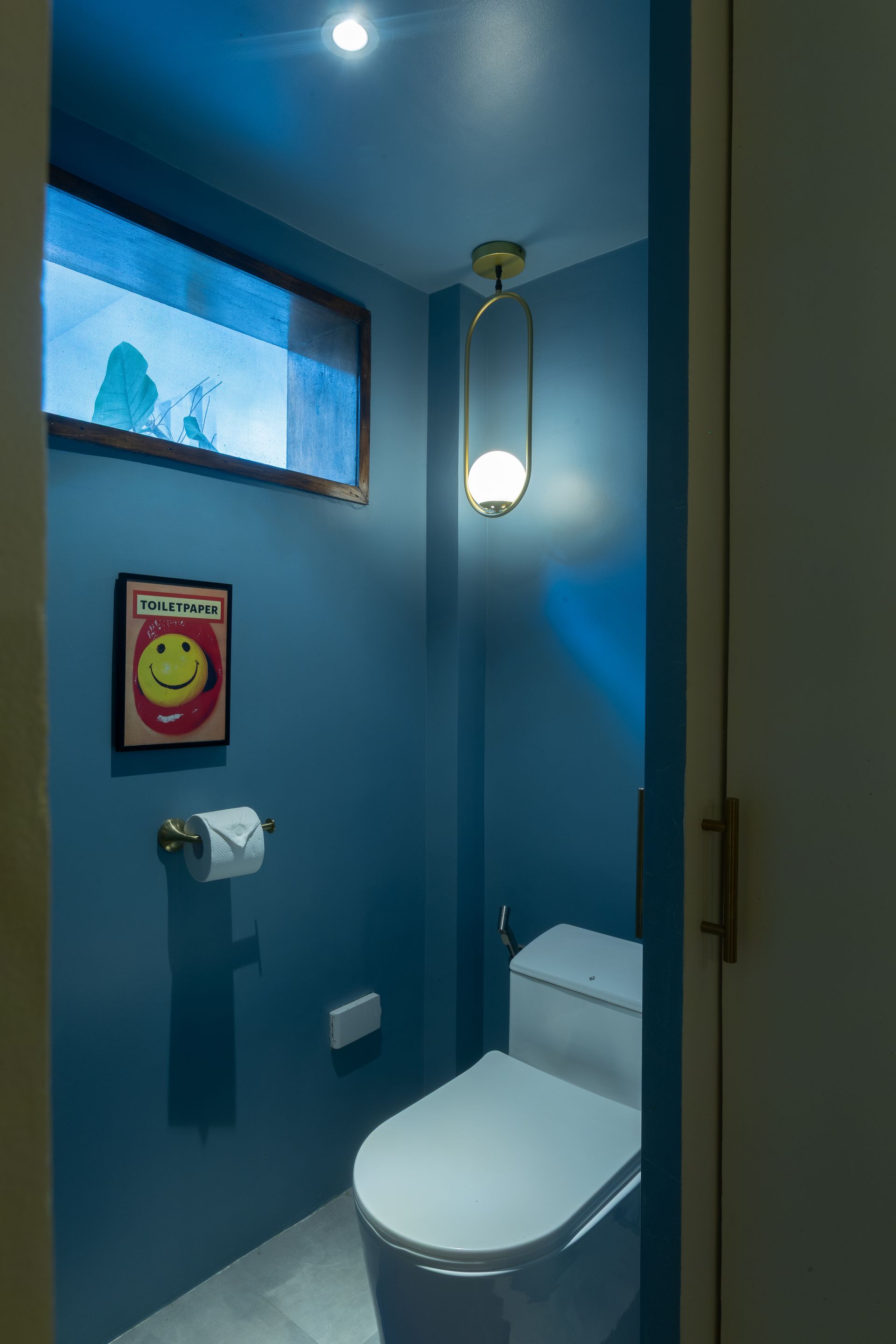 Small blue bathroom with a toilet, artwork, and a hanging light.
