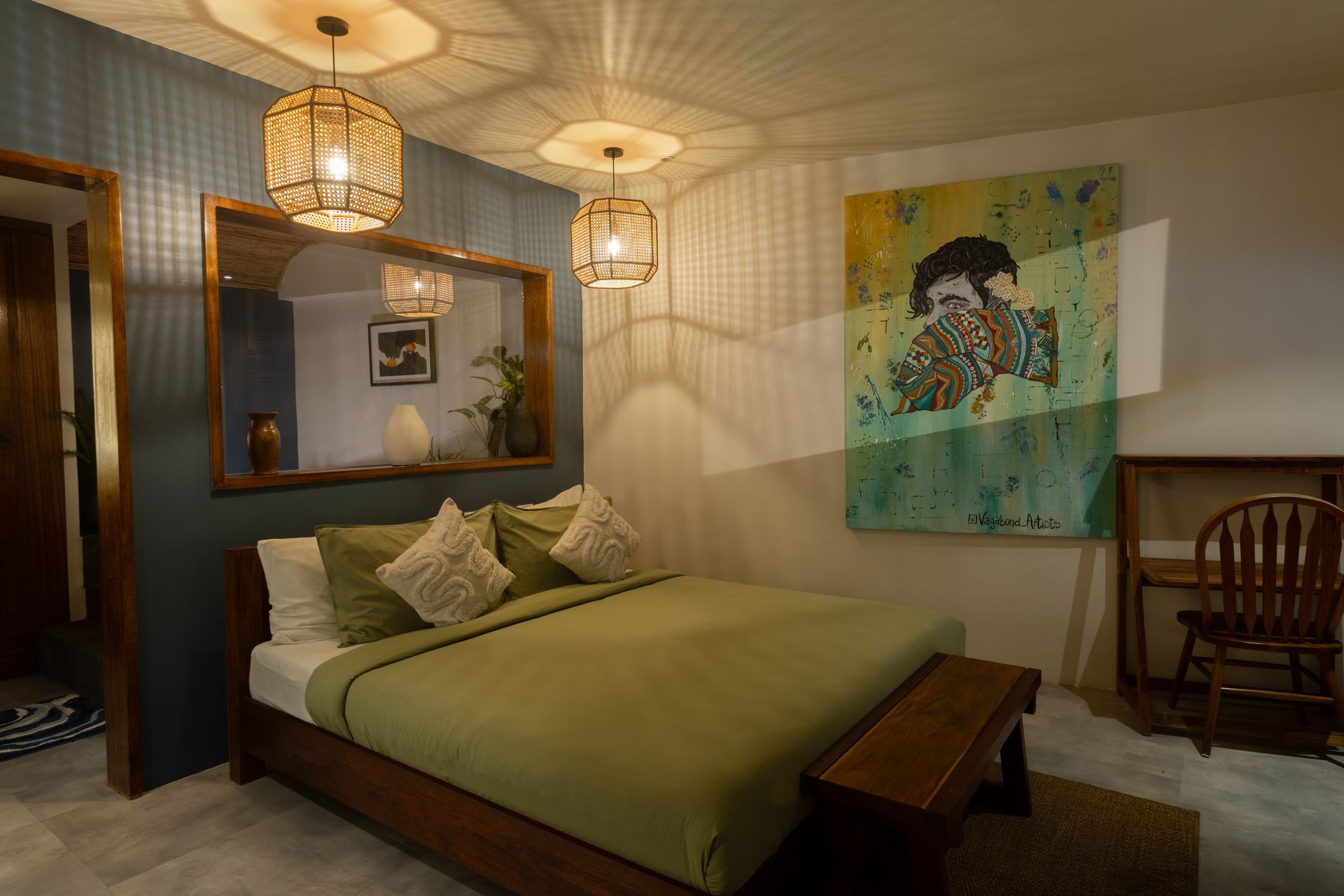 Bedroom with olive green bedding, large mirror, art, and rattan light fixtures.