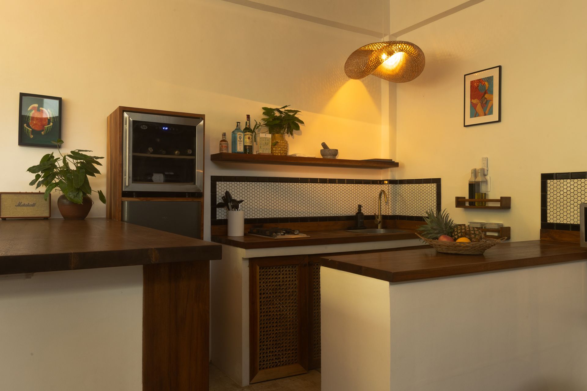 A corner kitchen with wooden counters and cabinets, a wine fridge, and decorative hanging light fixture.