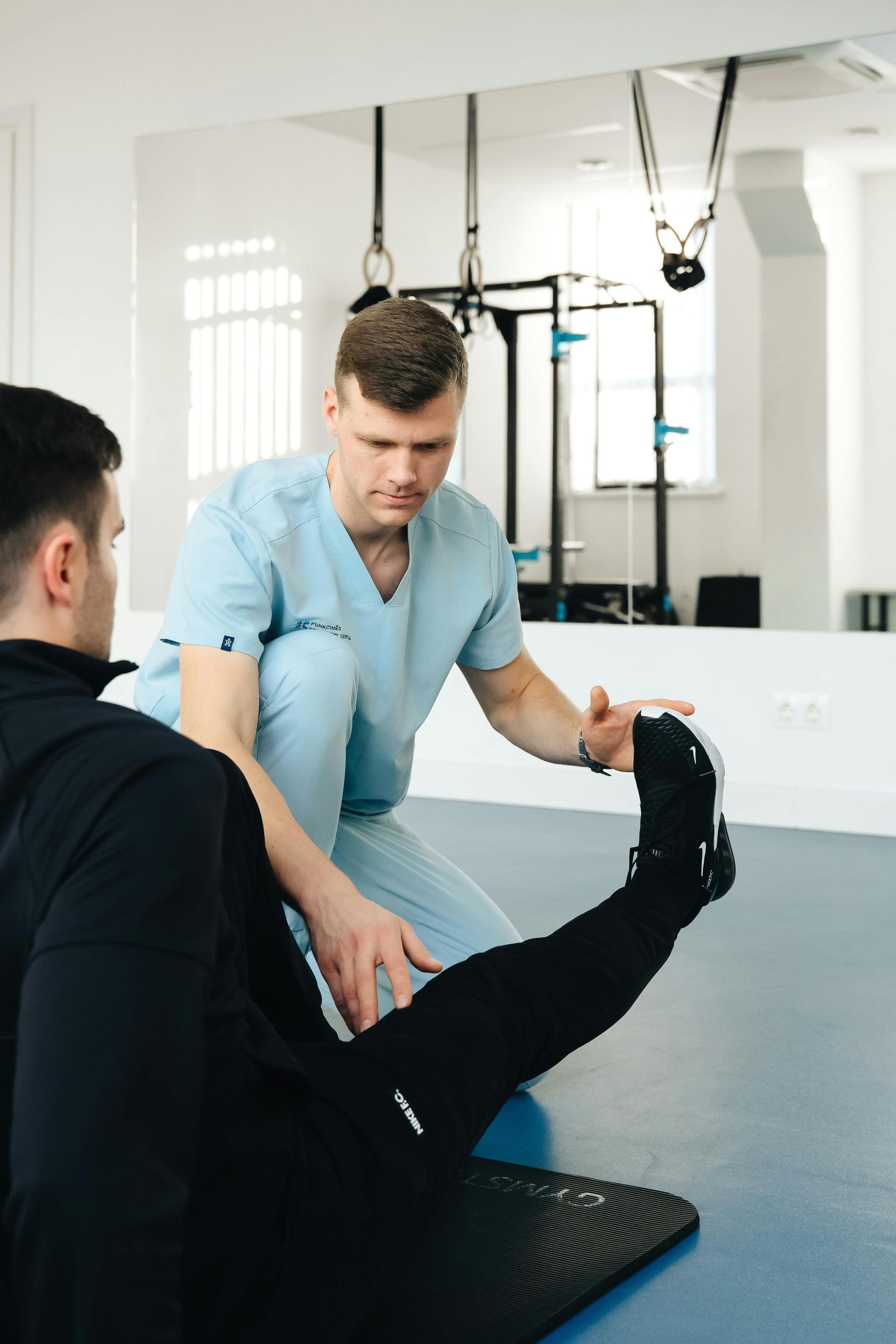 Physical therapist assisting a patient with leg stretching exercise in a bright therapy room.
