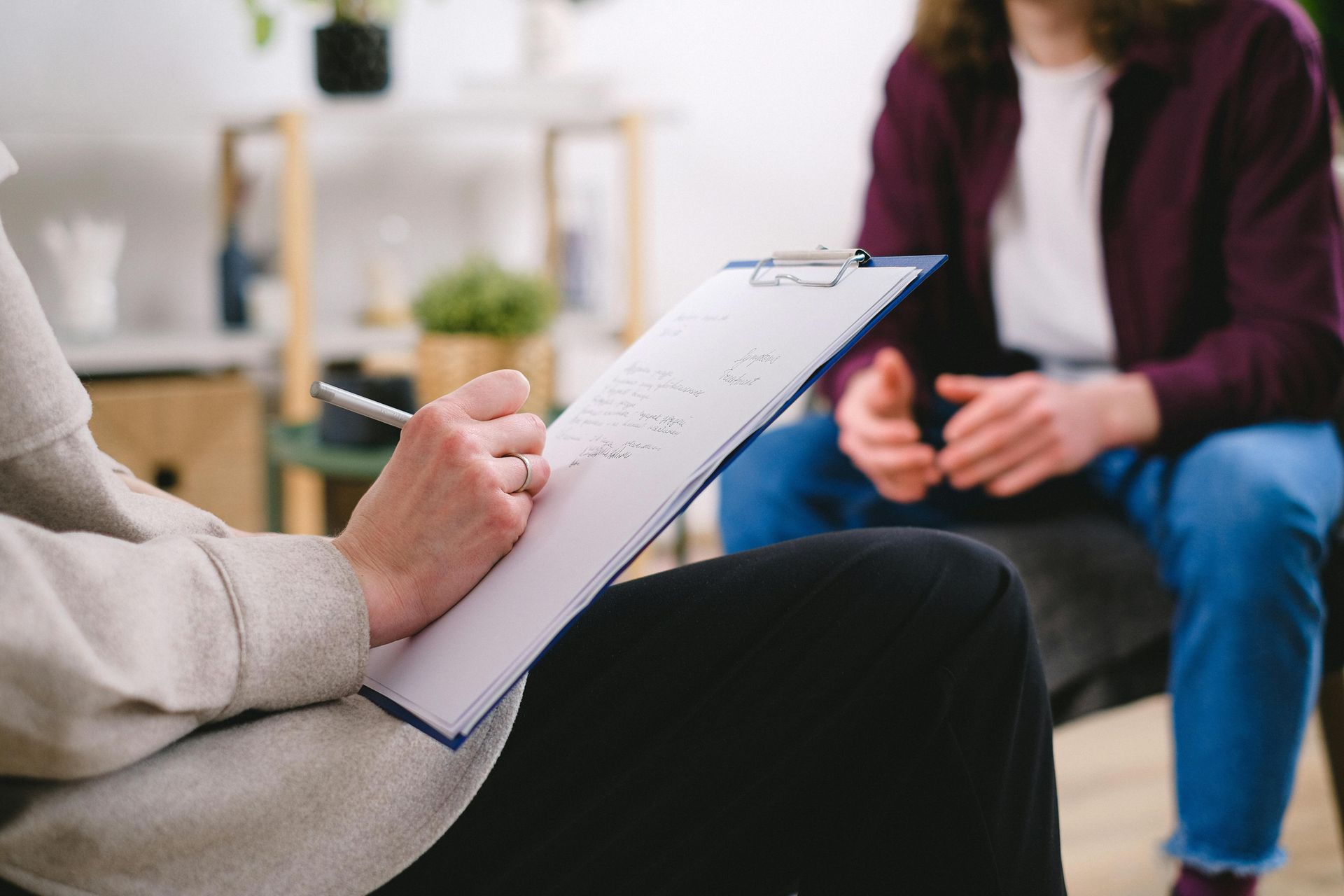 A therapist taking notes while a patient talks in a bright room.