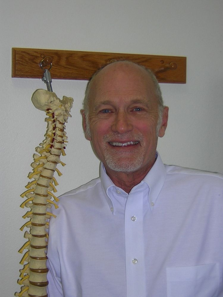 Smiling man in white shirt next to a model of a spine.