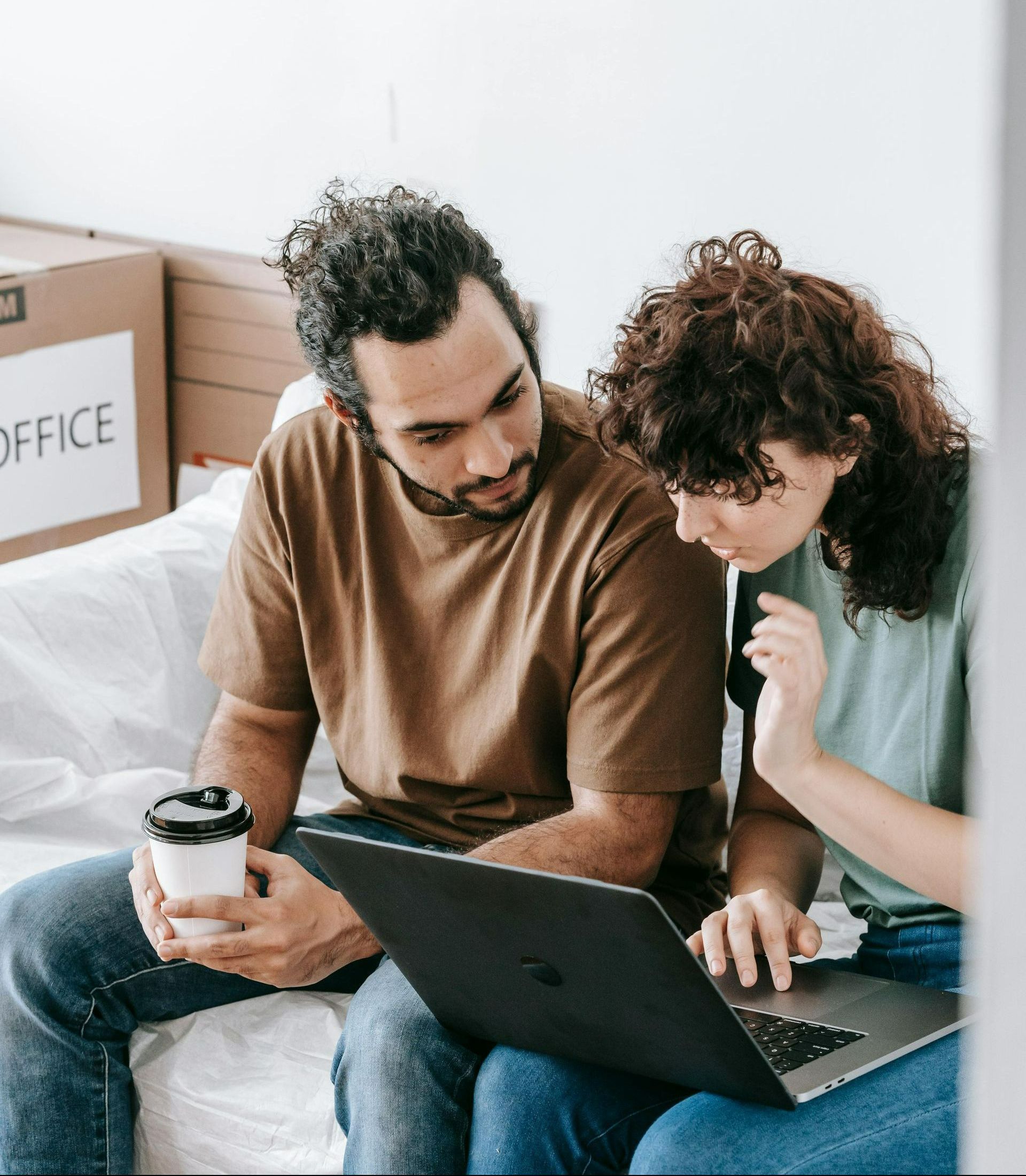 A man and a woman are sitting on a bed looking at a laptop.