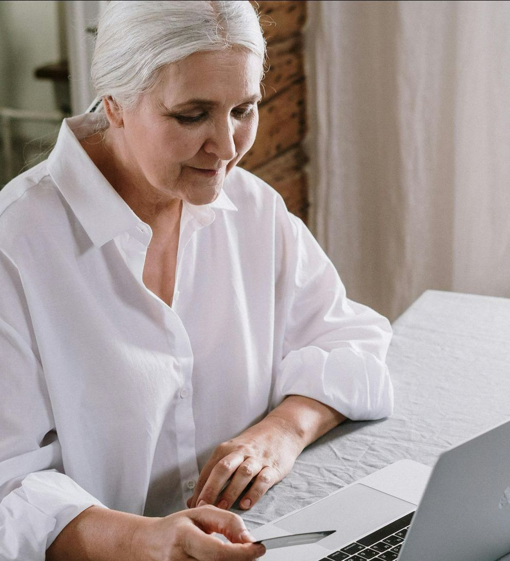 An older woman is sitting at a table using a laptop computer.