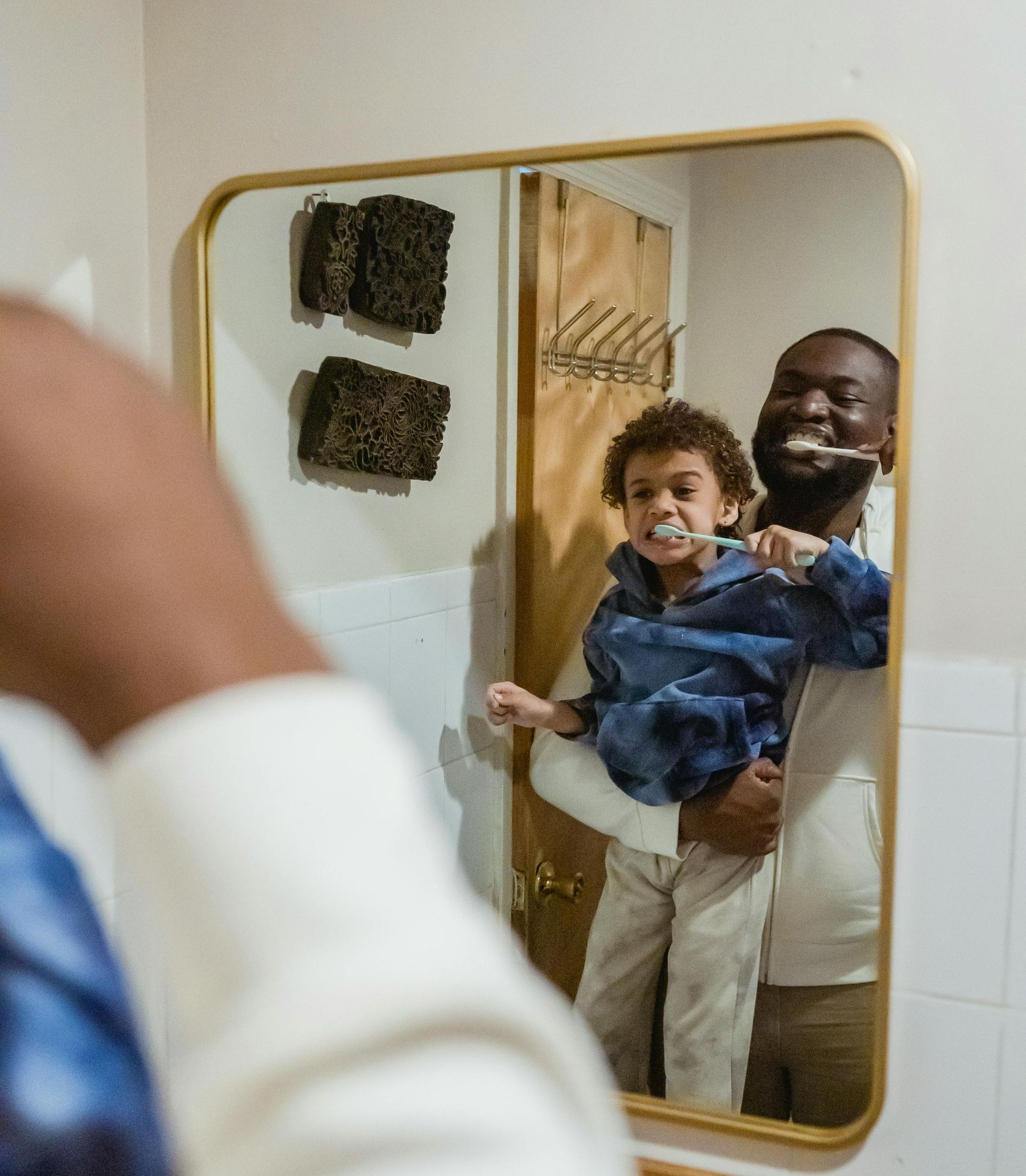 A man and a child are brushing their teeth in front of a mirror.