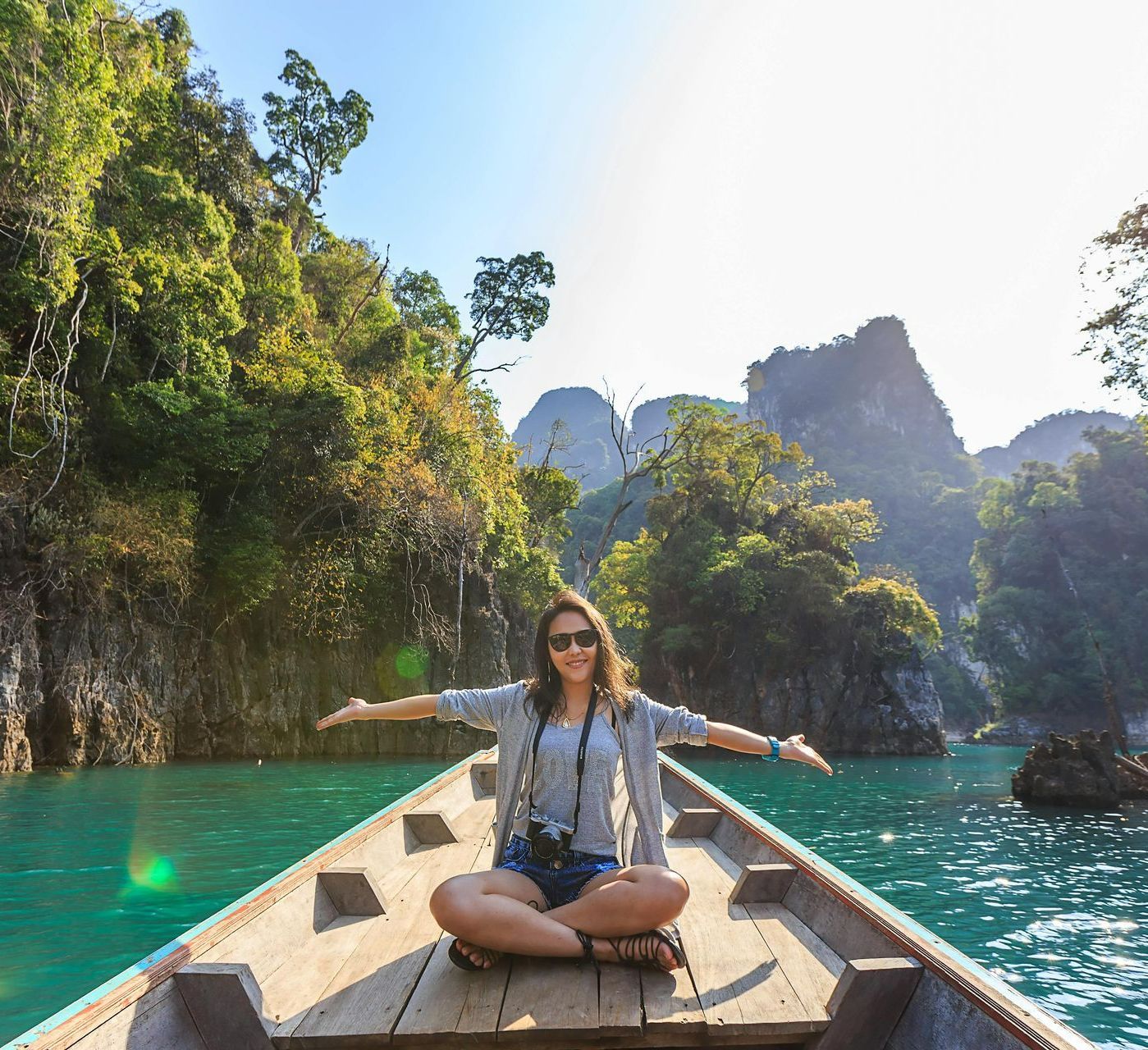 A woman is sitting in a boat on a lake with her arms outstretched.