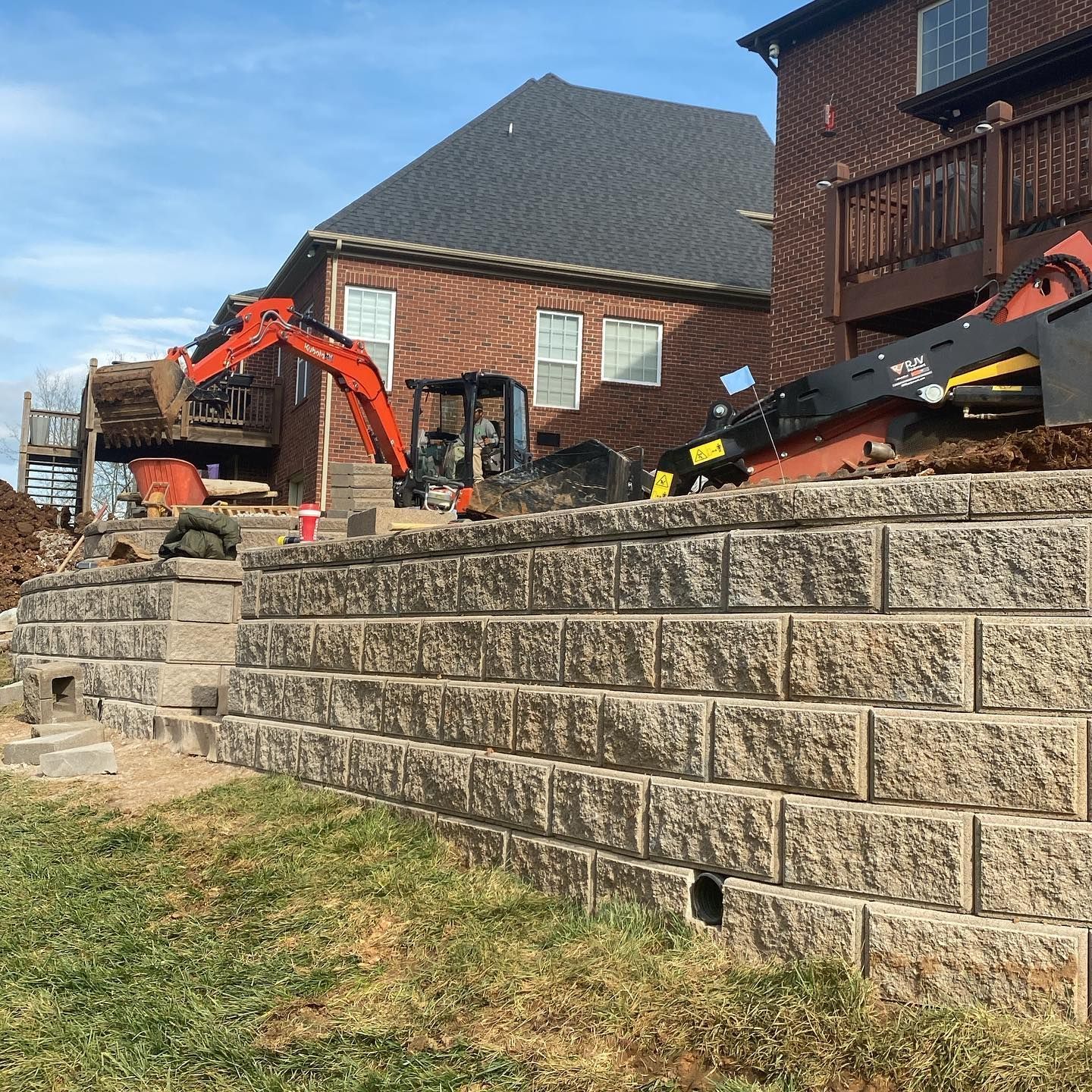 A brick wall is being built in front of a brick house.