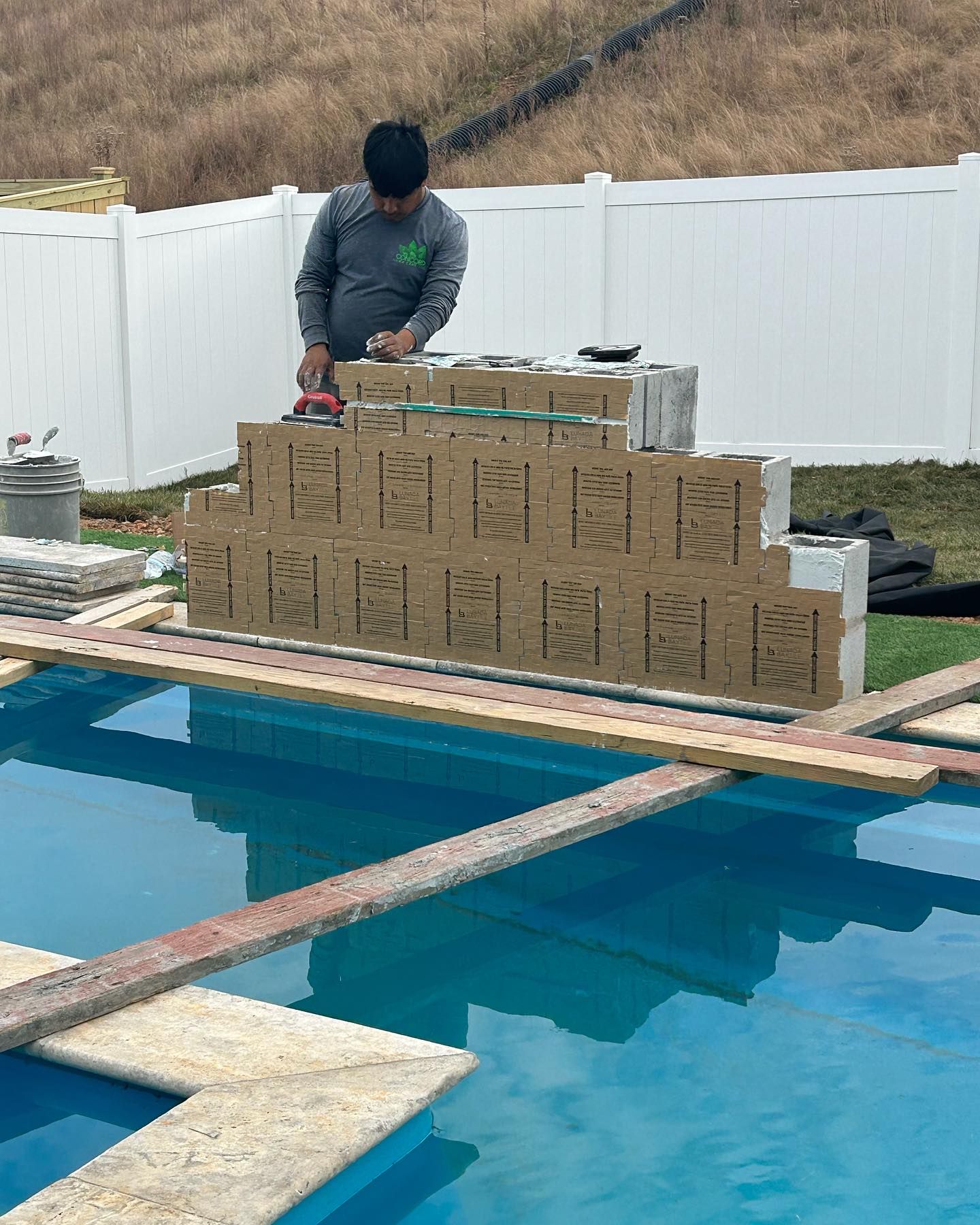A man is standing next to a stack of cardboard boxes next to a pool.