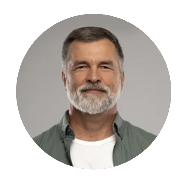 Man with gray beard, smiling, wearing a green shirt over a white t-shirt, against a gray background.