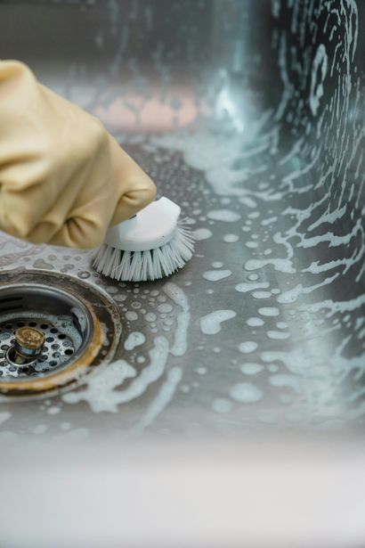 Gloved hand scrubbing a soapy kitchen sink drain with a brush