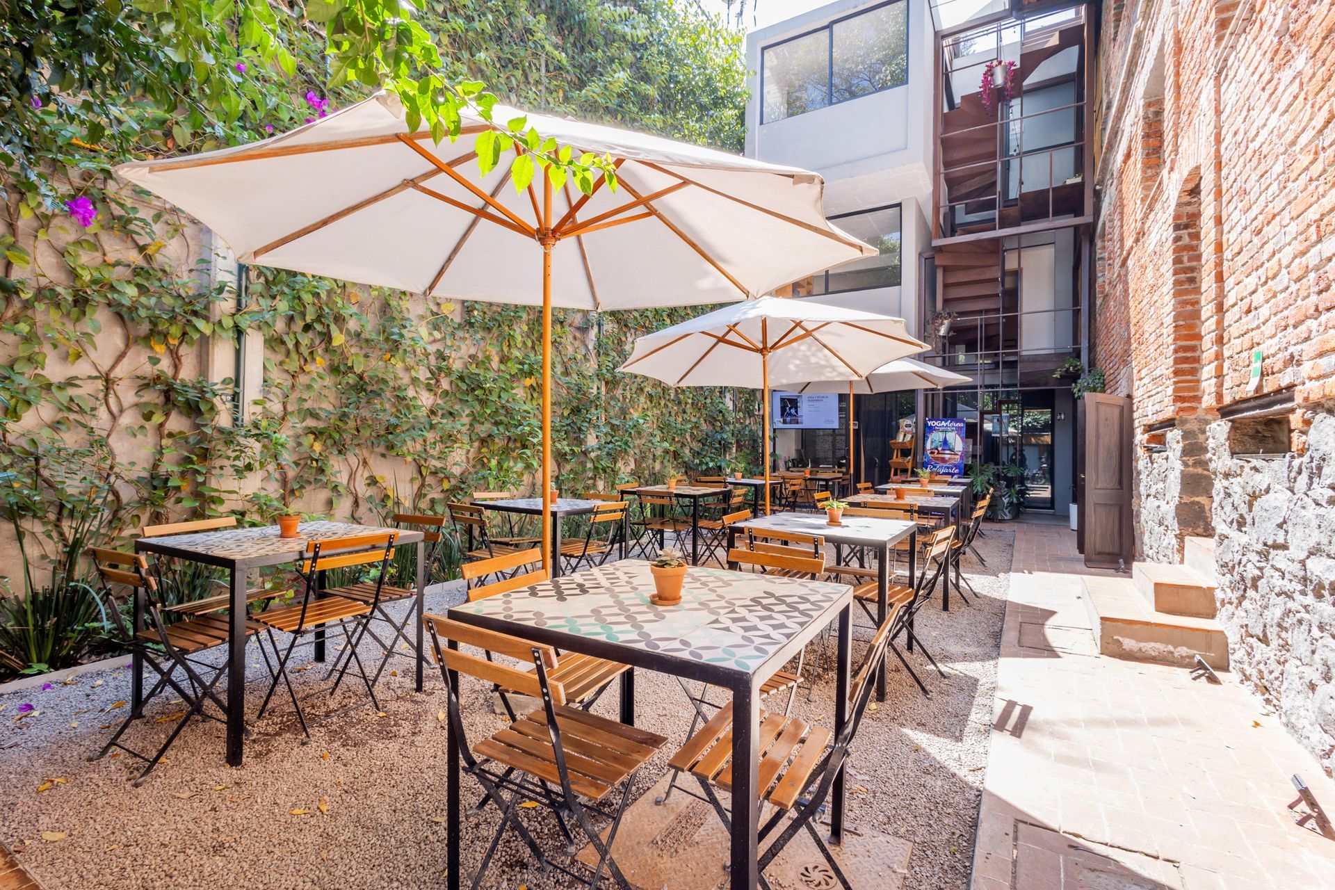 Un patio con mesas y sillas y sombrillas frente a un edificio.