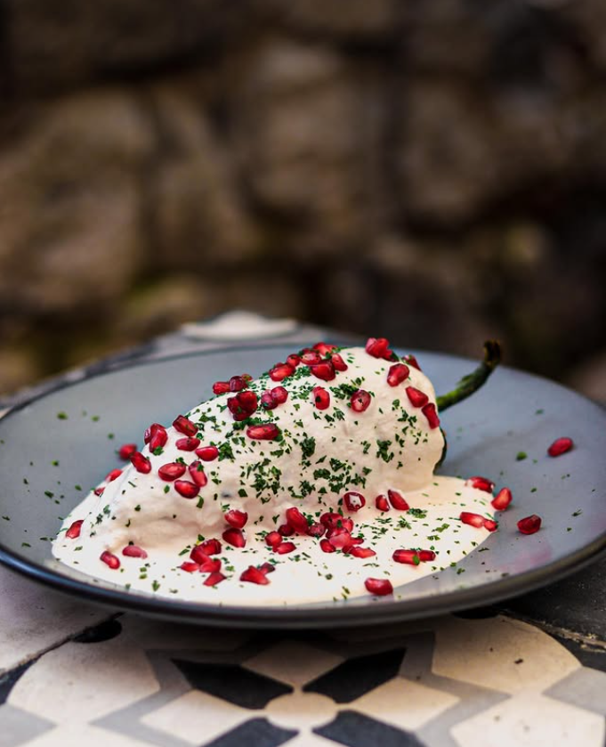 Un pimiento cubierto de salsa blanca y semillas de granada en un plato.