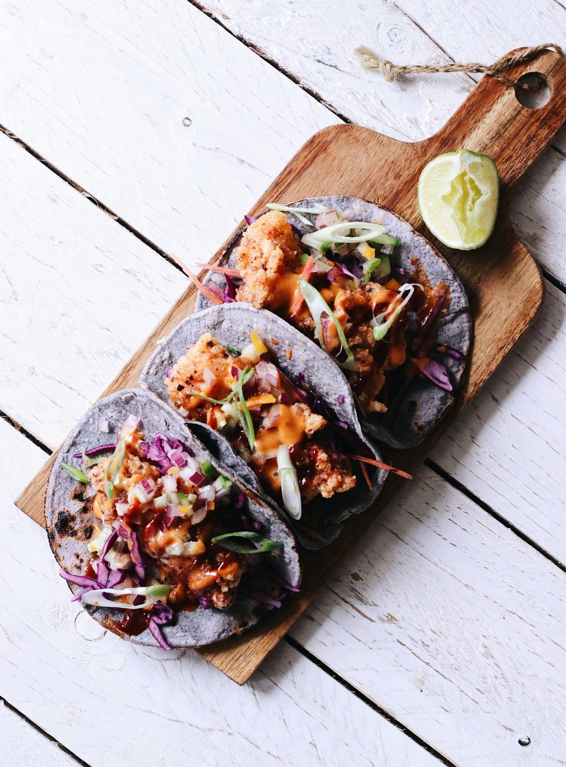 Hay tres tacos sobre una tabla de cortar de madera sobre una mesa.