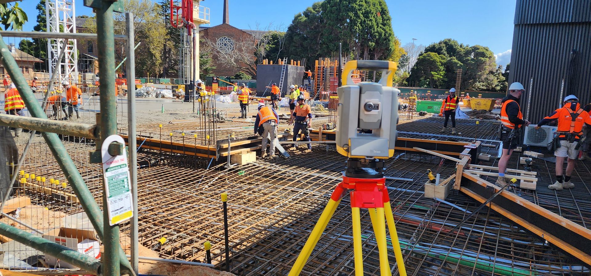 A group of construction workers are working on the  construction site for the Brighton Grammar Redevelopment project, a survey instrument in the foreground.