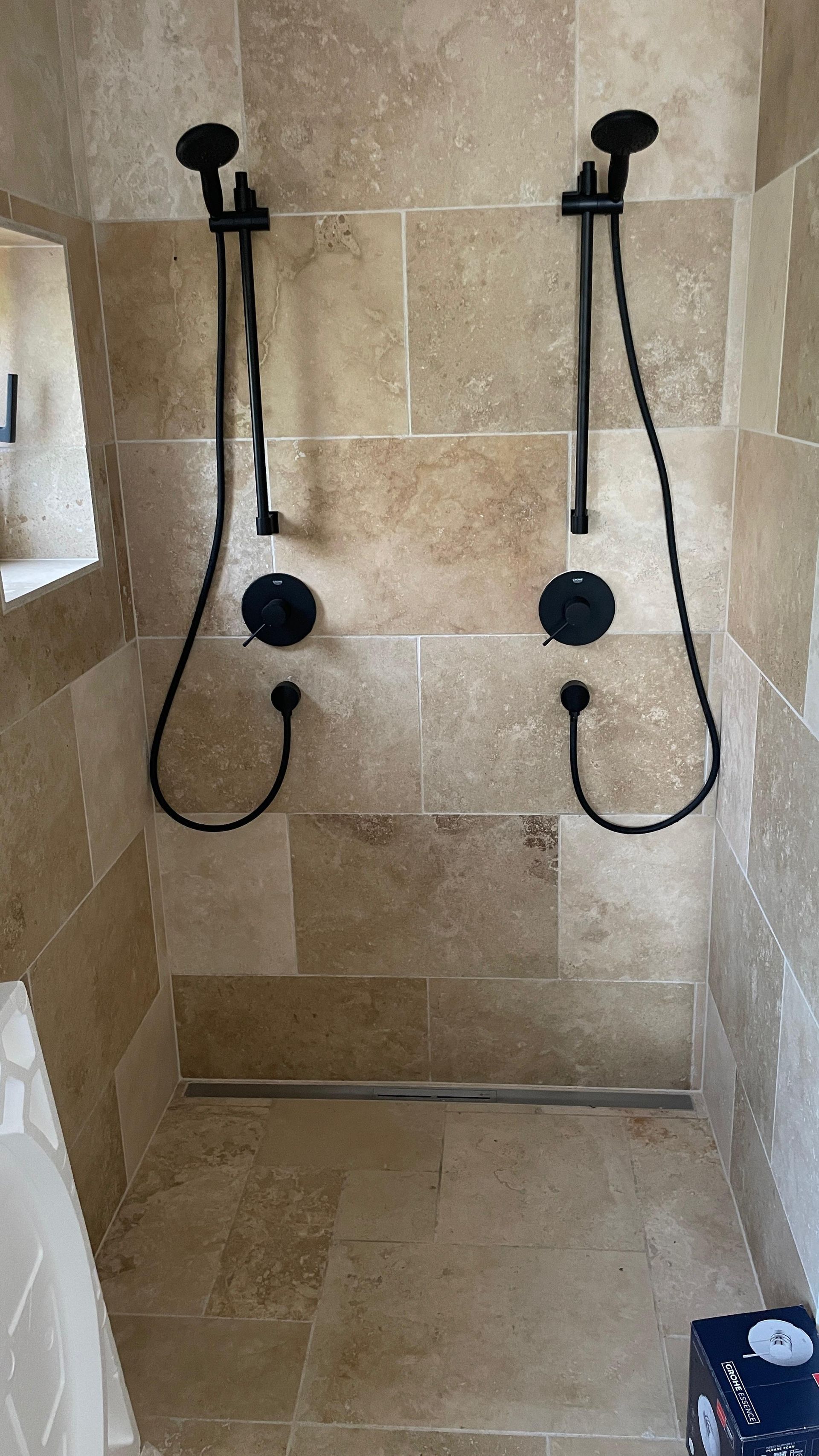 Zwei schwarze Duschköpfe und Armaturen an einer hellbraunen Fliesenwand.