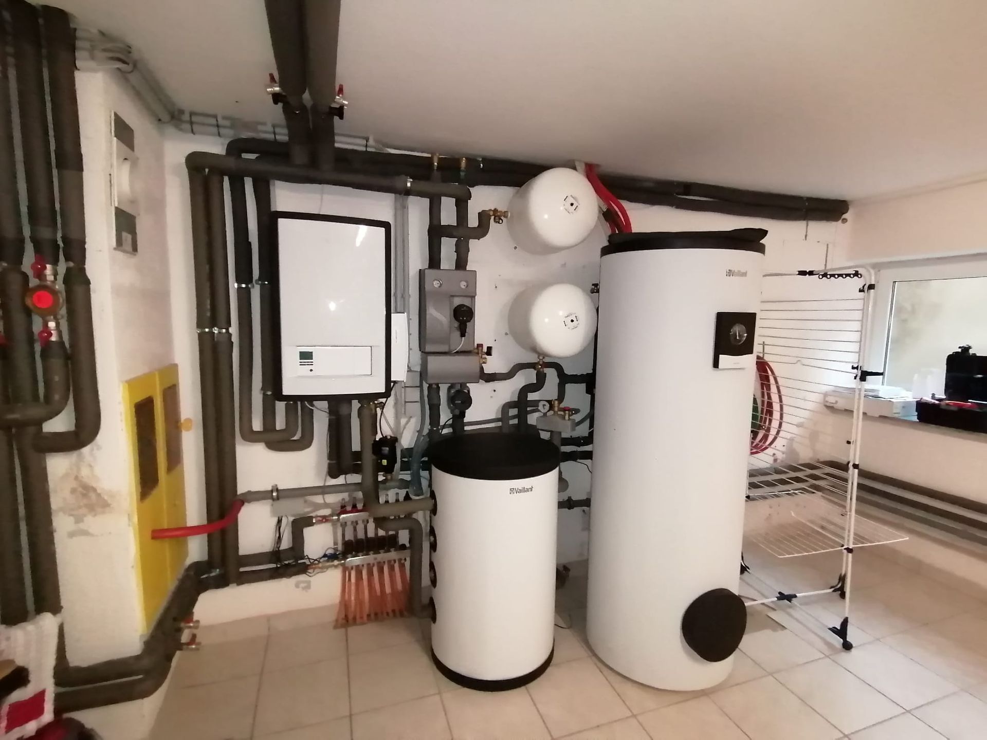 Heizungsanlage im Keller mit weißen Tanks, Rohren und Bedienfeld.