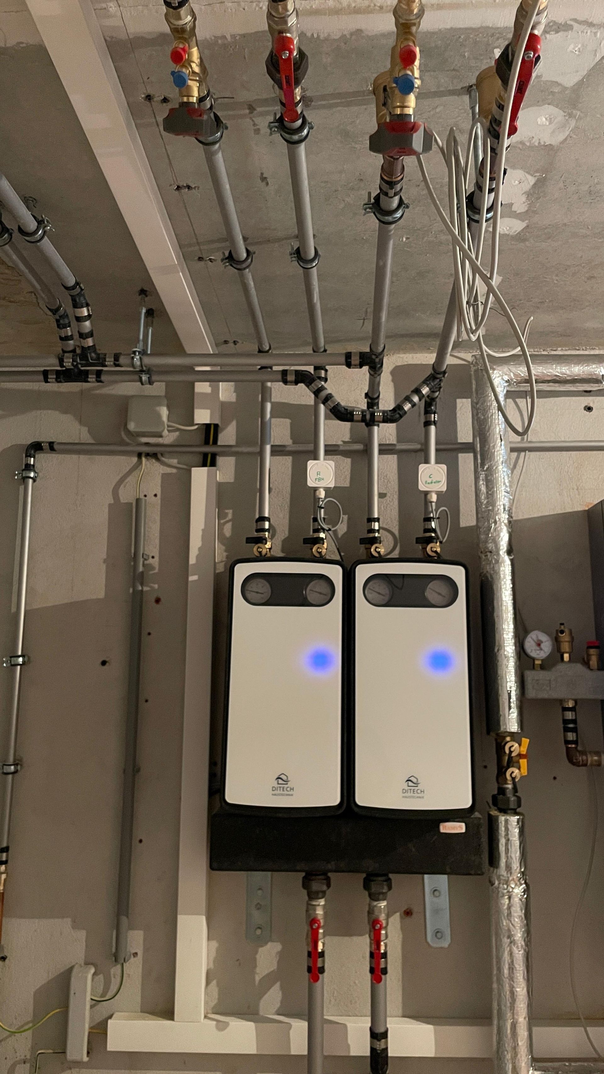 Zwei weiße, an der Wand montierte Energieeinheiten mit blauen Leuchten, die Rohre an einer Betonwand angeschlossen sind.
