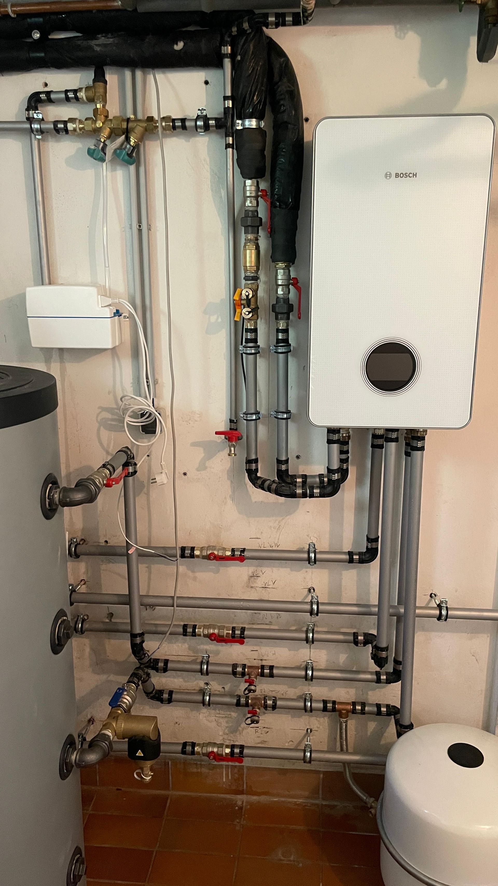 Rohre und ein weißes Haushaltsgerät an einer Wand mit einem Wassertank.