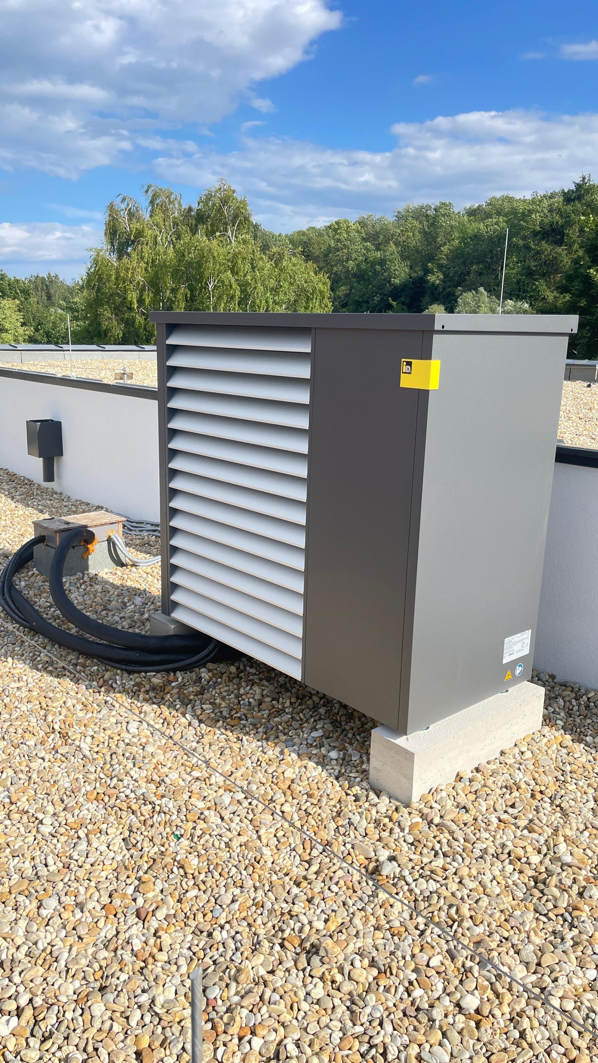 Klimaanlage auf einem Kieseldach, graues und braunes Metall, neben einer weißen Wand und schwarzen Rohren.