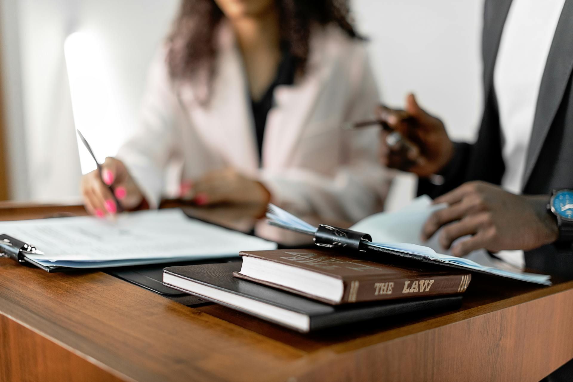 Two people reviewing documents, one writing. A book labeled