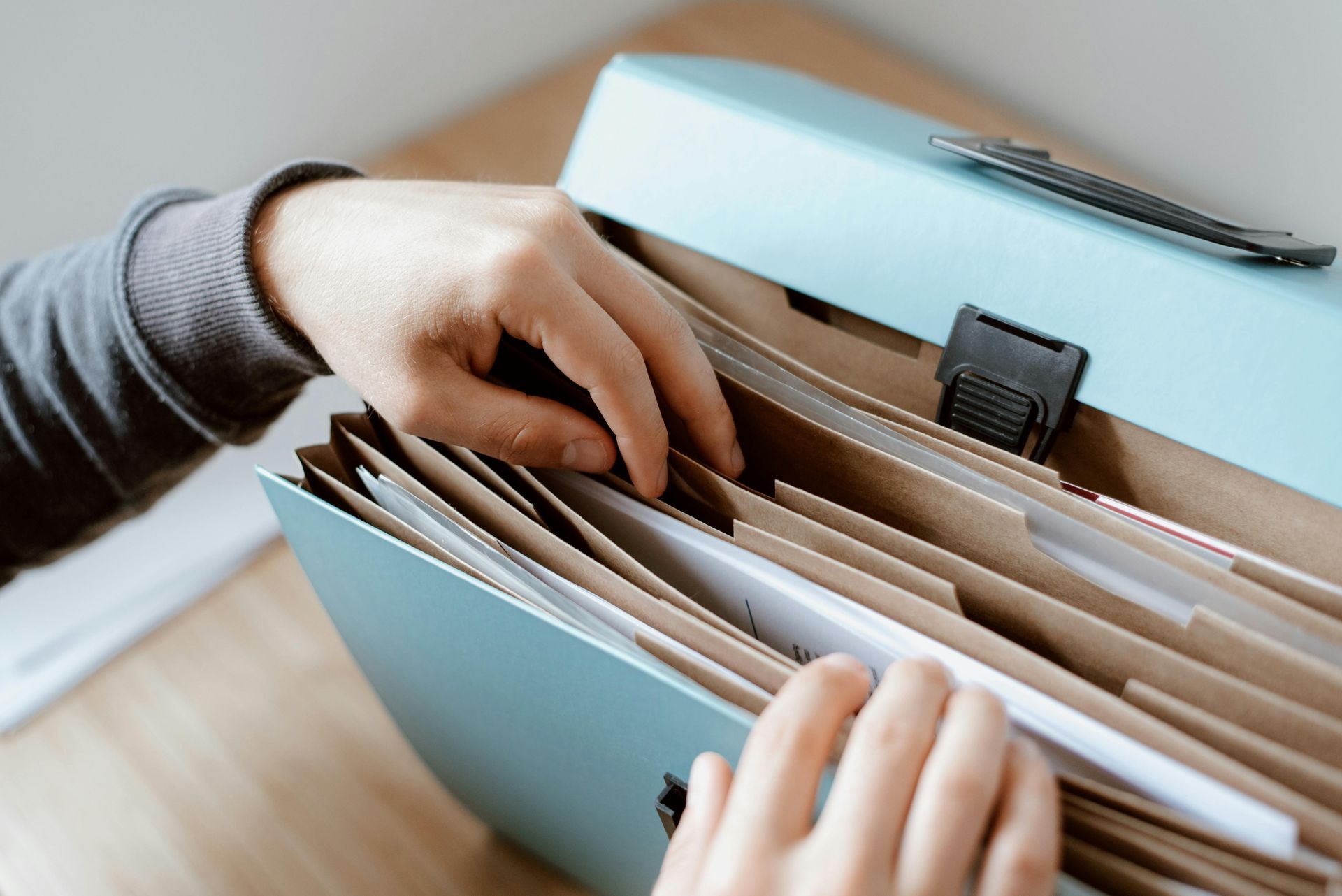 Hands sorting papers in a blue file box on a desk