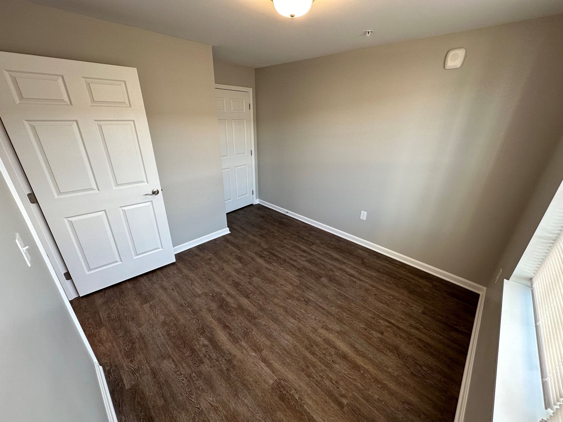 An empty bedroom with hardwood floors and a white door.