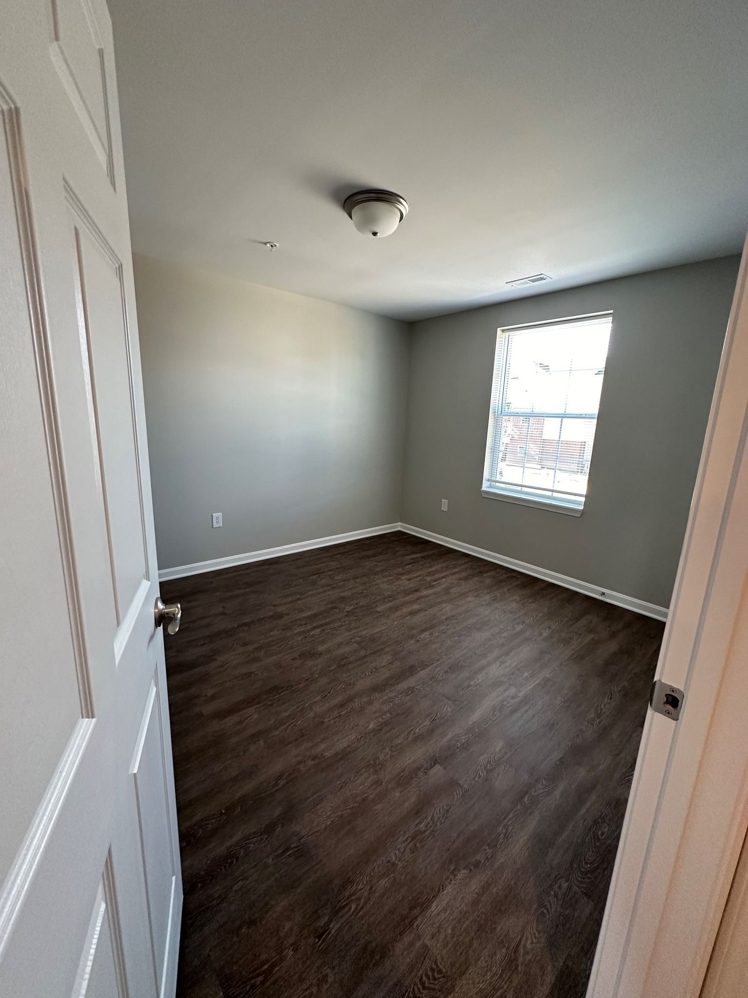An empty bedroom with hardwood floors and a window.