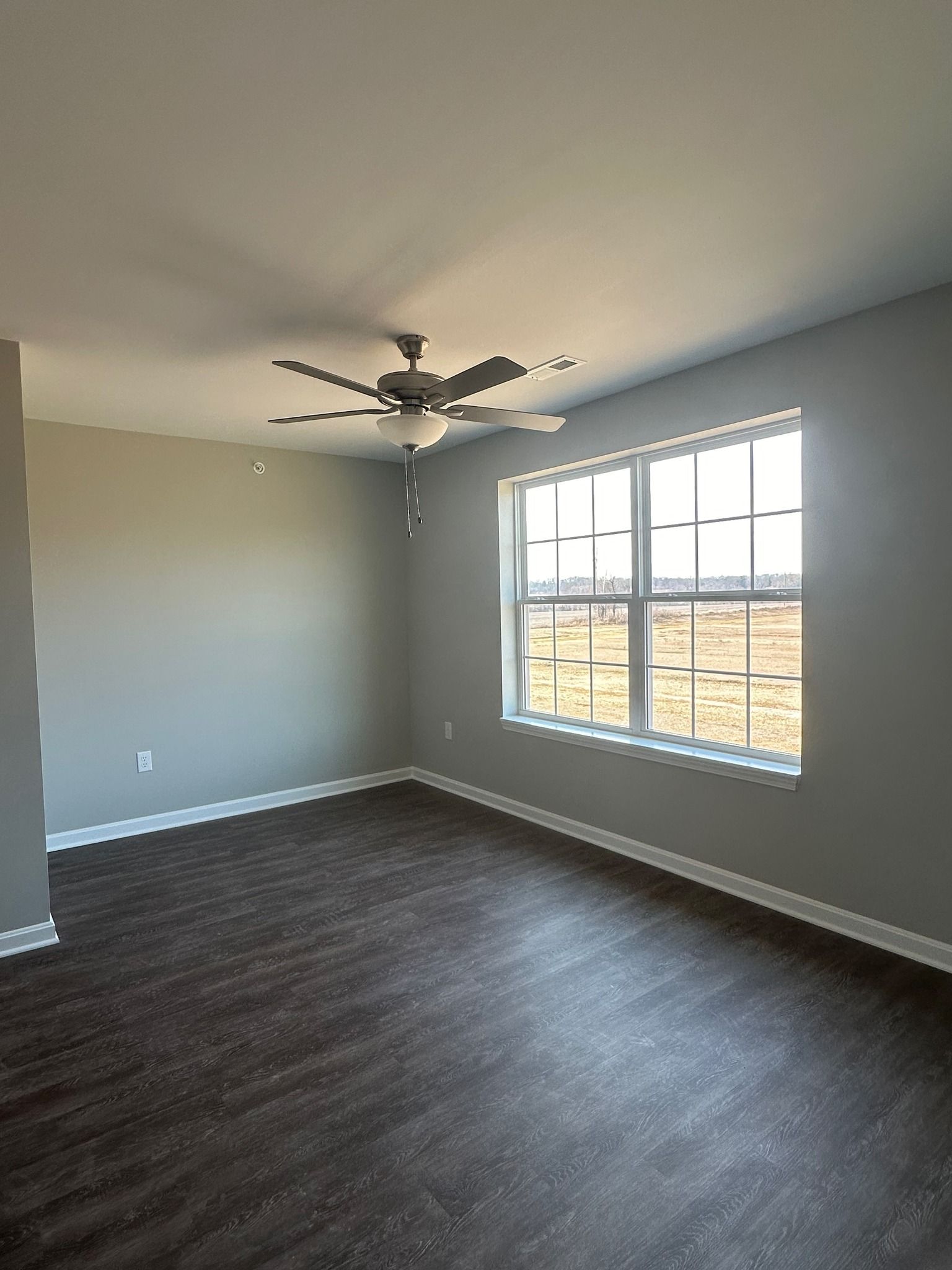 An empty living room with a ceiling fan and a large window.