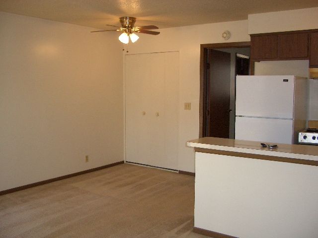 An empty room with a ceiling fan and a refrigerator