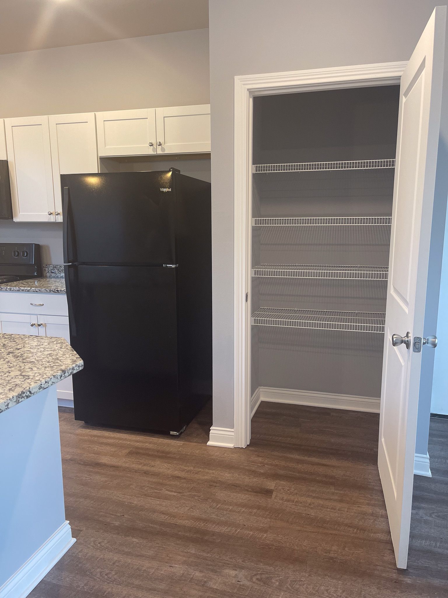 A kitchen with a black refrigerator and a pantry with shelves.