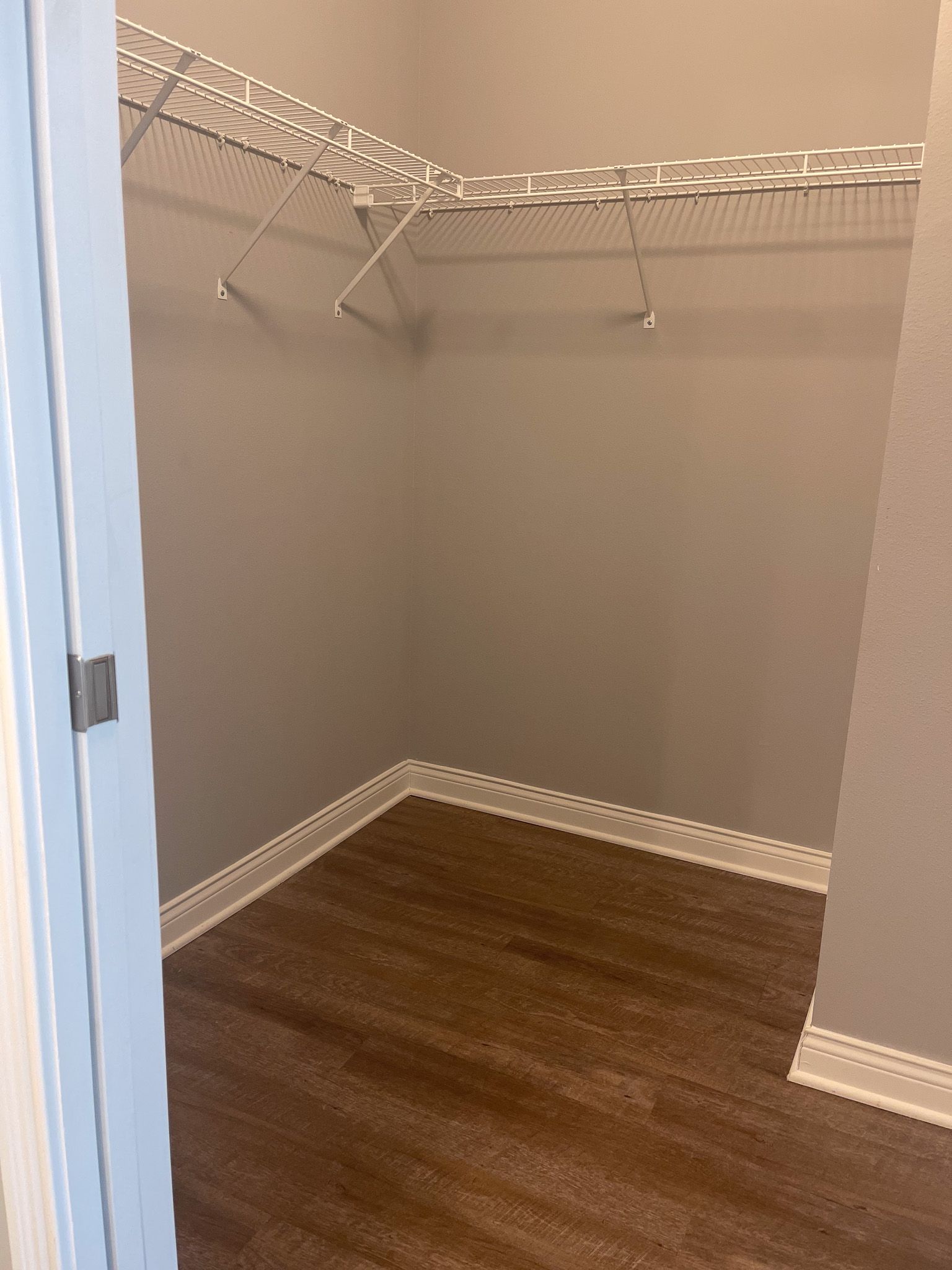 An empty walk in closet with hardwood floors and a white wire rack.