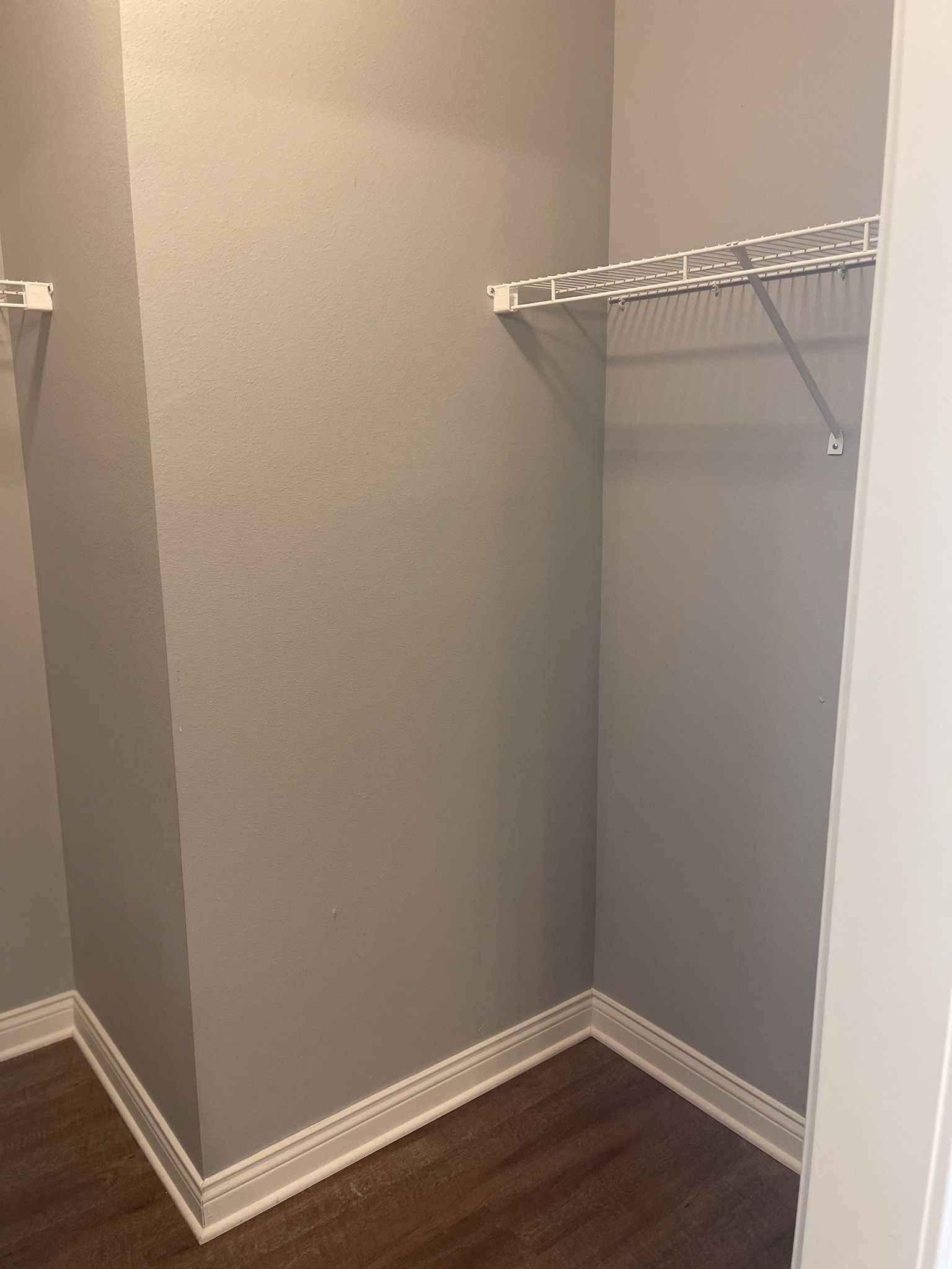 An empty walk in closet with a wooden floor and gray walls.
