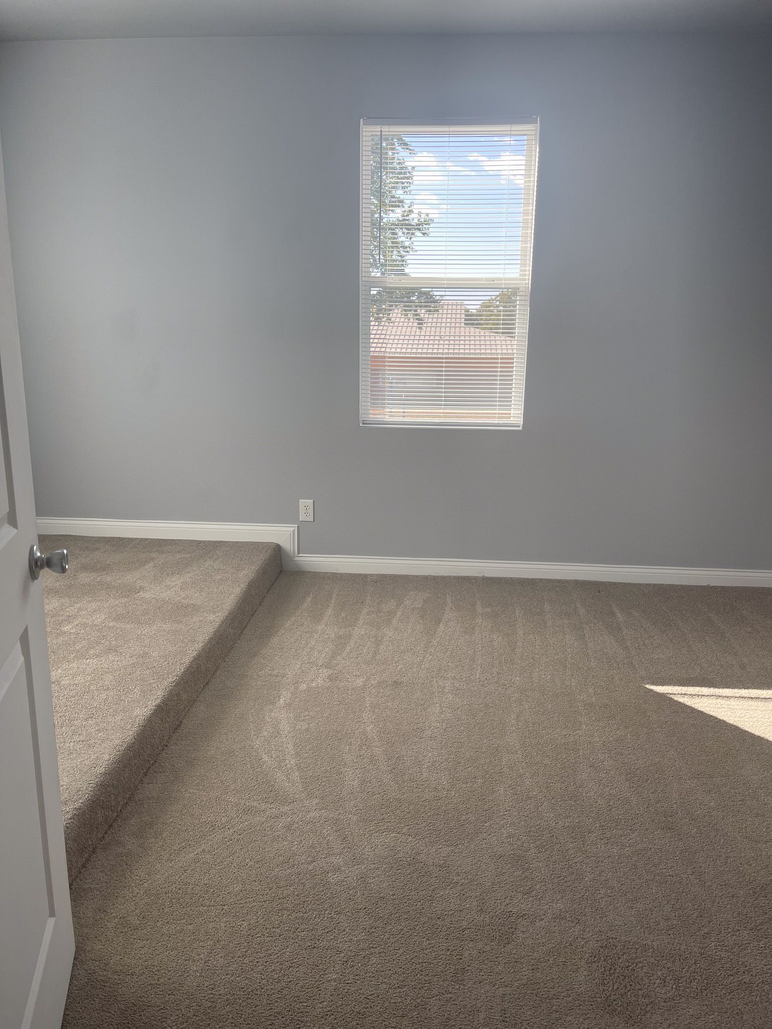 An empty room with a window and a carpeted floor.