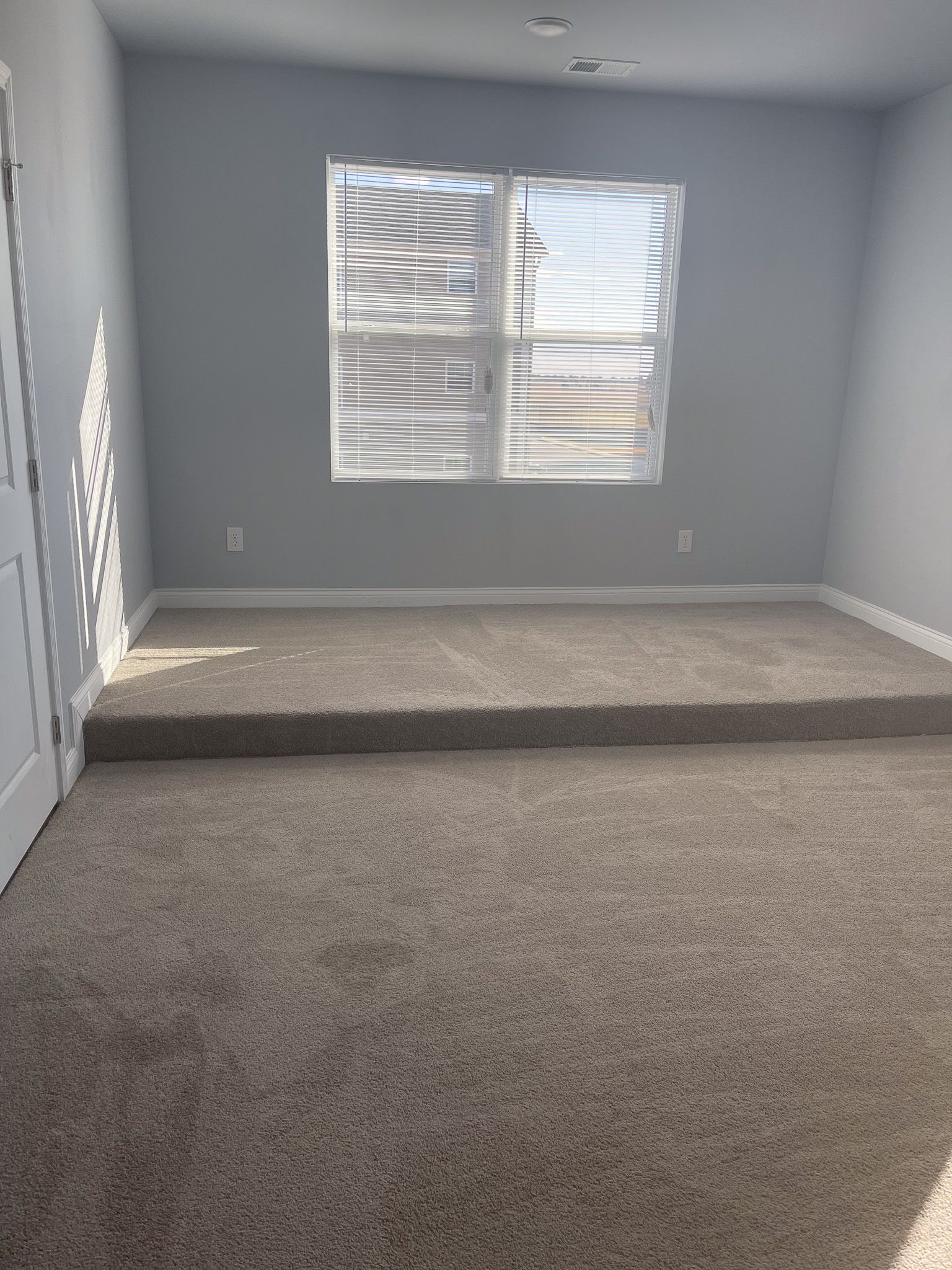 An empty room with a carpeted floor and a window.