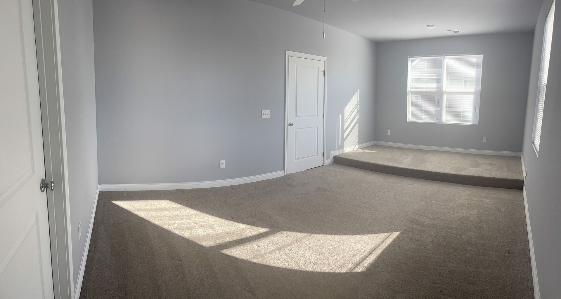 A large empty room with a carpeted floor and two windows.