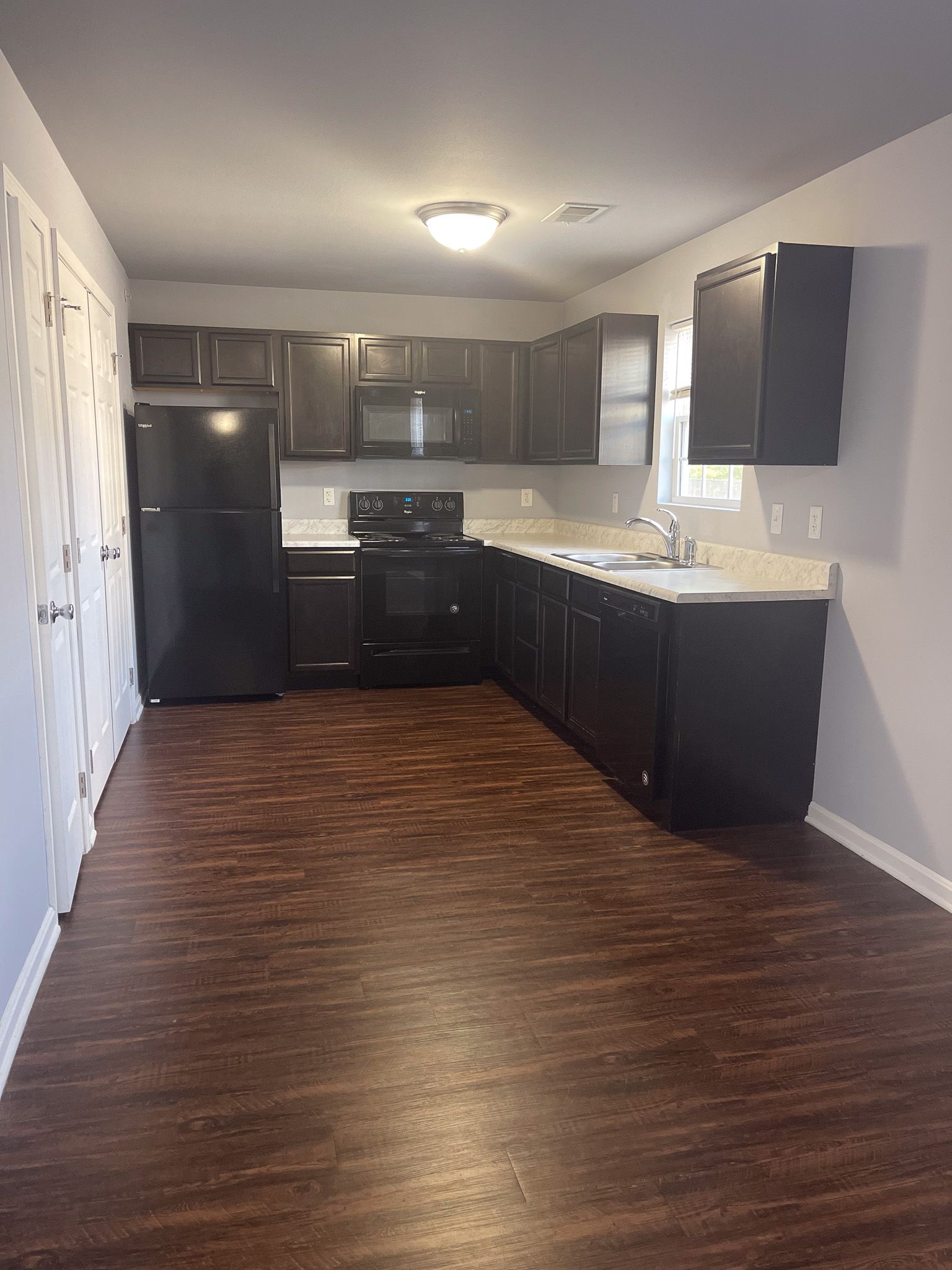 A kitchen with black cabinets , a black refrigerator , a stove , and a sink.