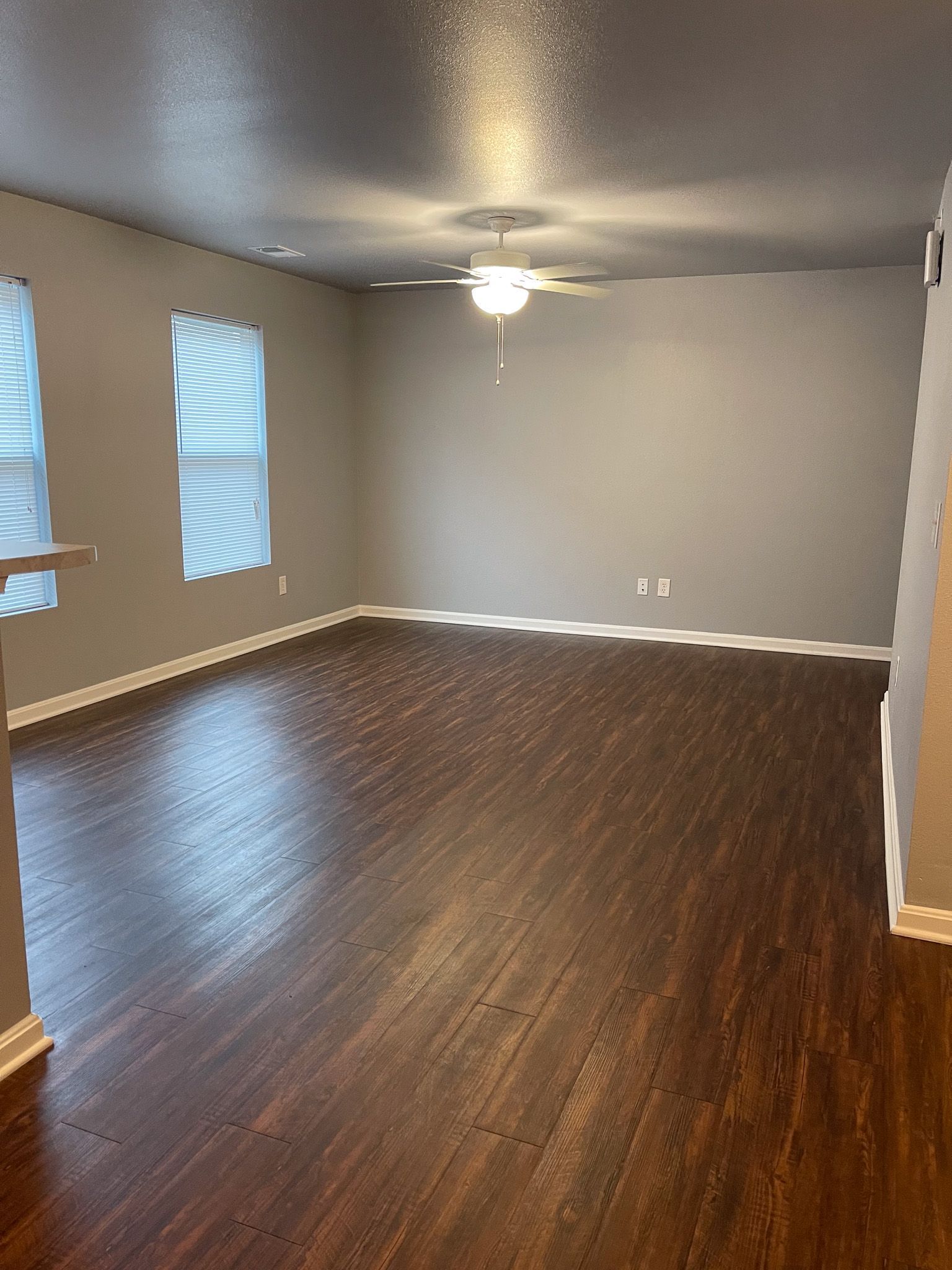 An empty living room with hardwood floors and a ceiling fan.