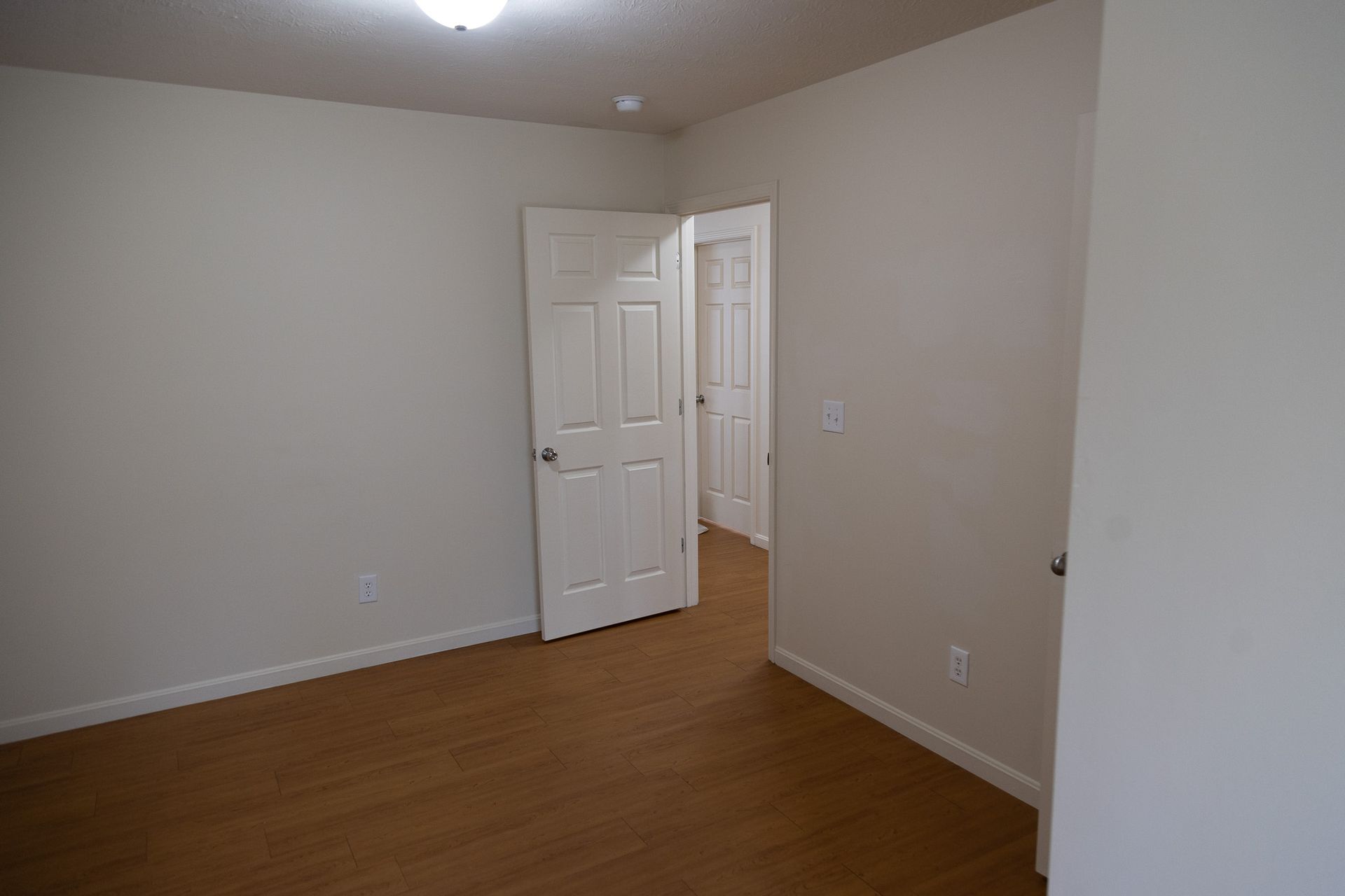 An empty bedroom with two doors and a light on the ceiling.